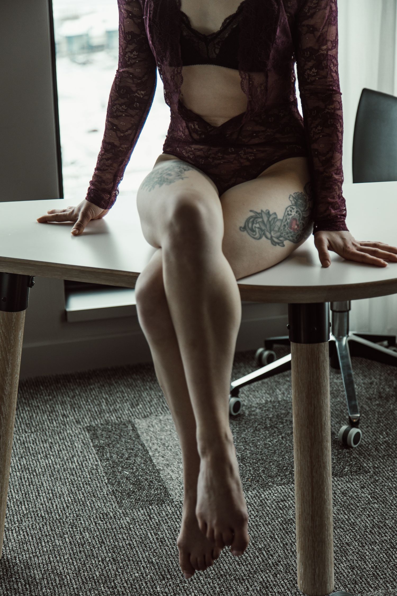 Close-up of bare legs dangling from a desk edge against carpeted floor.