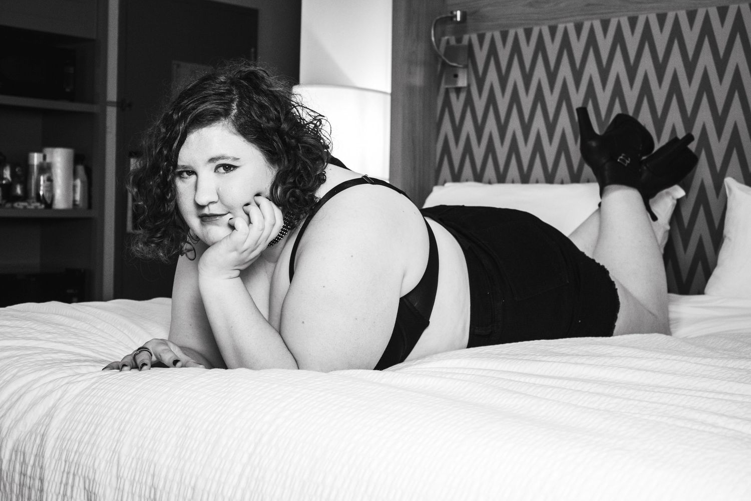 Intimate boudoir photo of person relaxing on white bedding in black lingerie.
