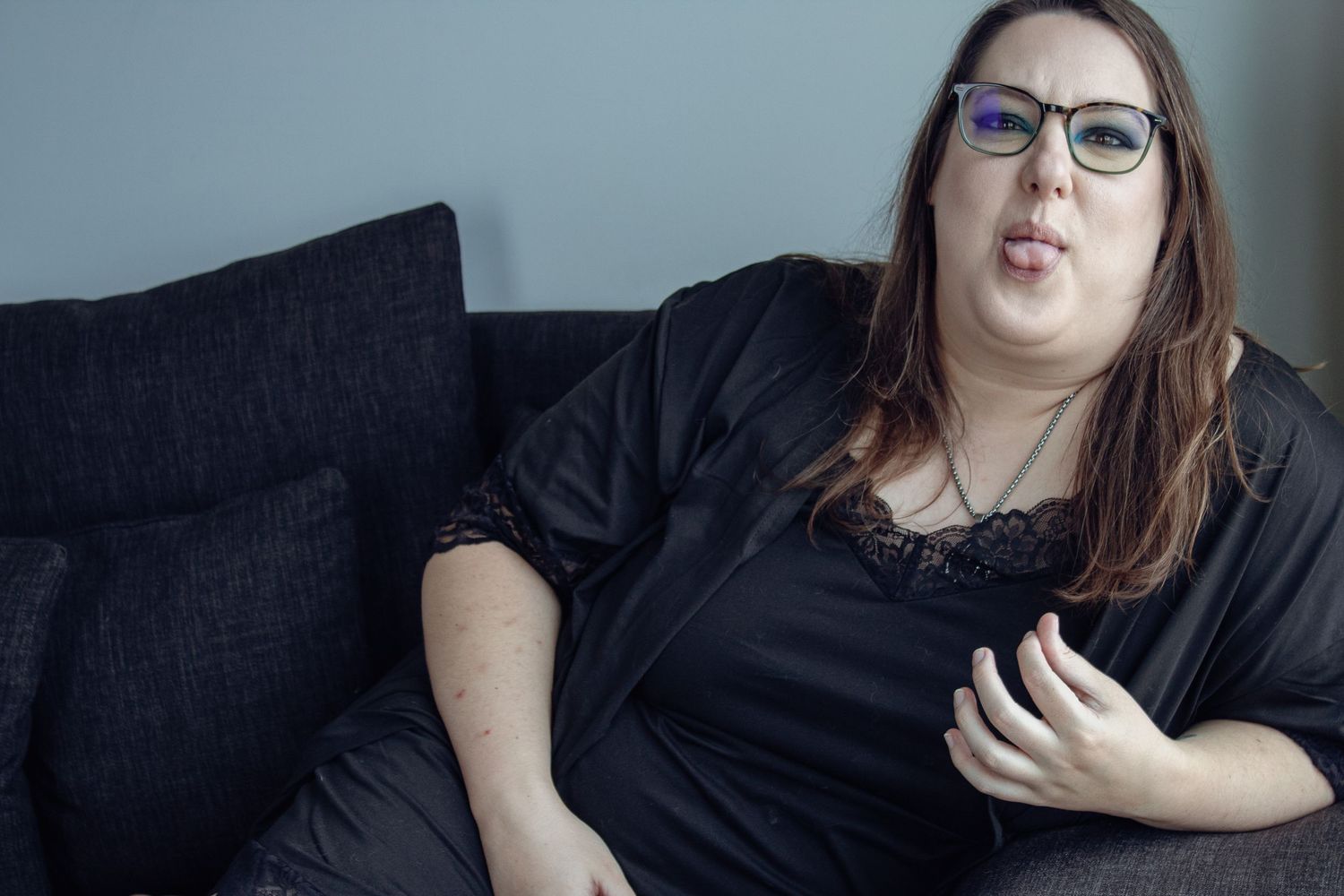 A relaxed figure wearing glasses and black attire reclines on a dark couch.