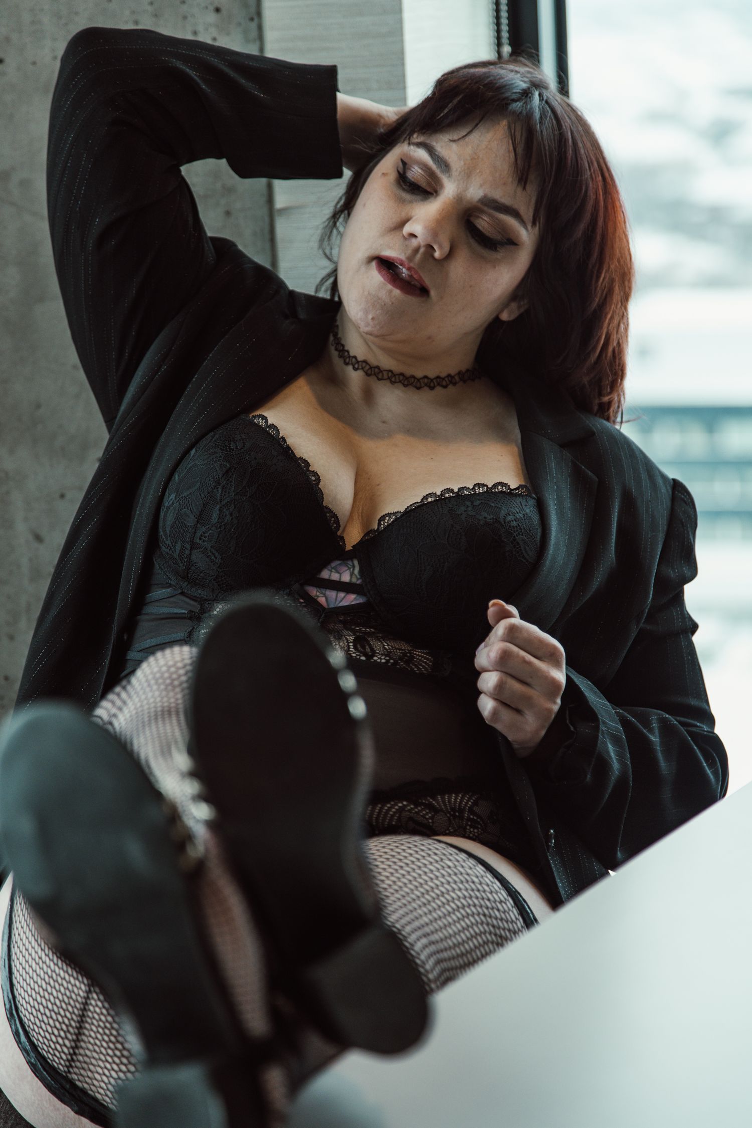 Moody fashion portrait by window featuring black lingerie and cardigan ensemble.