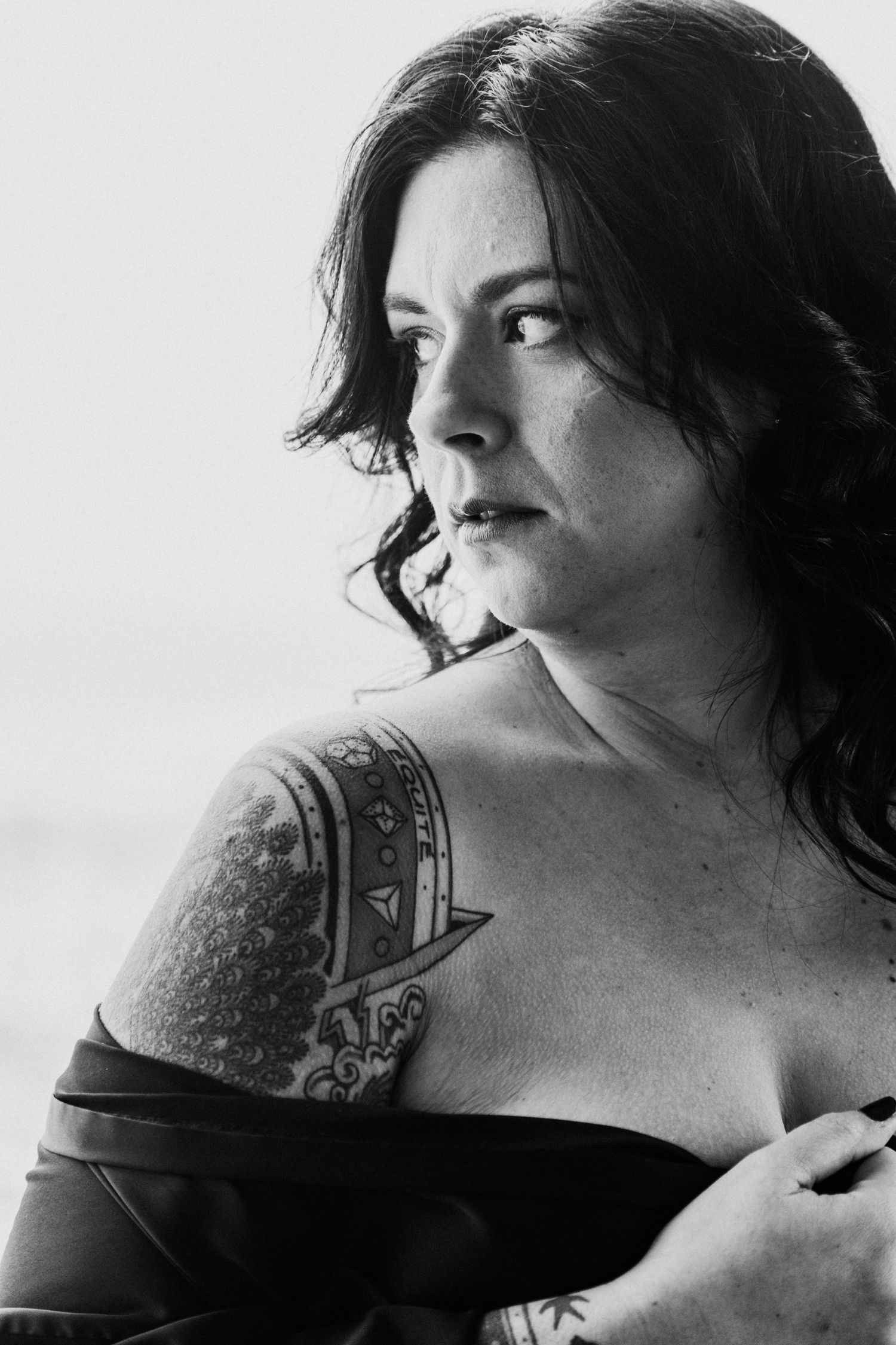 Black and white artistic portrait showing shoulder tattoos and dark hair.