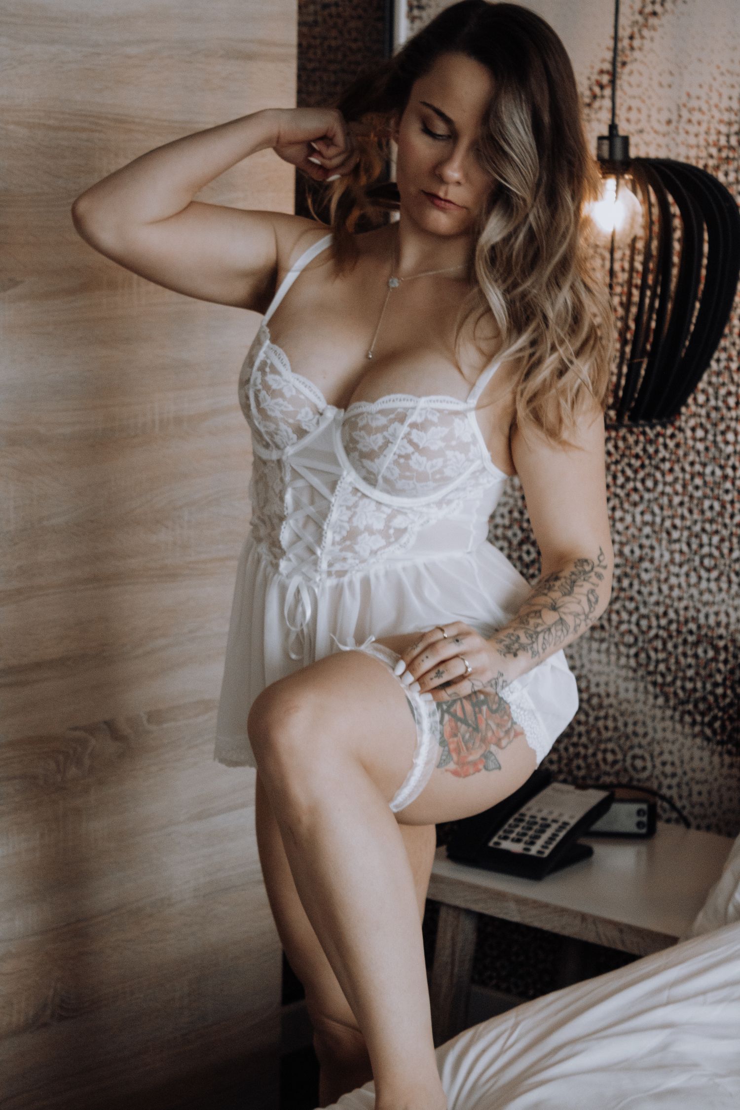 Intimate boudoir photo featuring white lace lingerie and tattoo details in moody lighting.