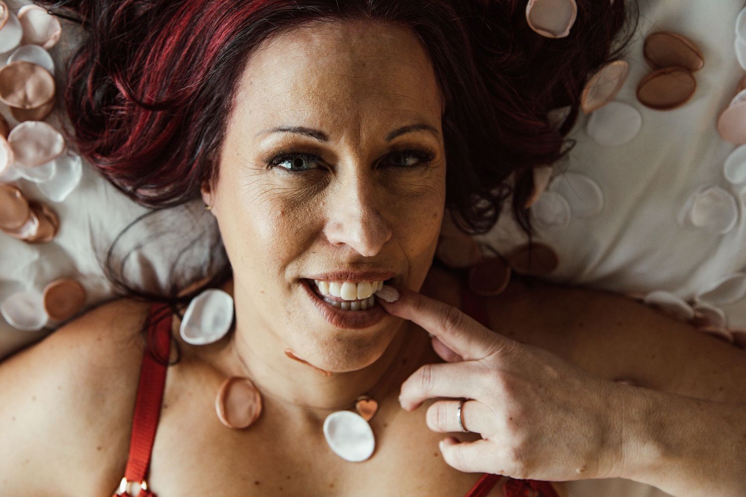 Artistic boudoir portrait with rose petals scattered on white bedding.