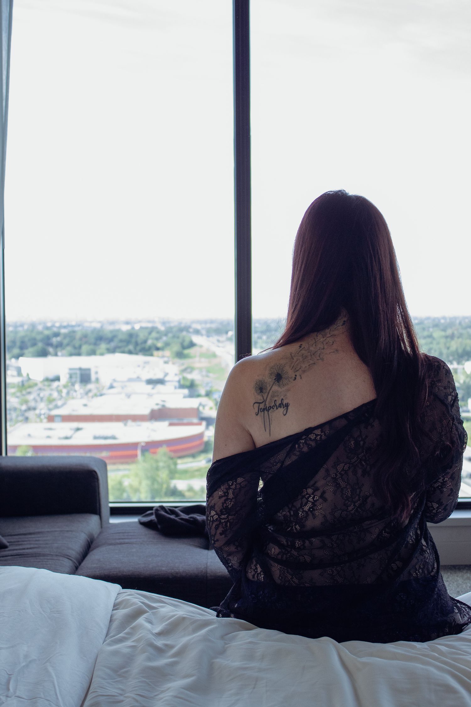 Silhouette of person in black lace against window with city view.