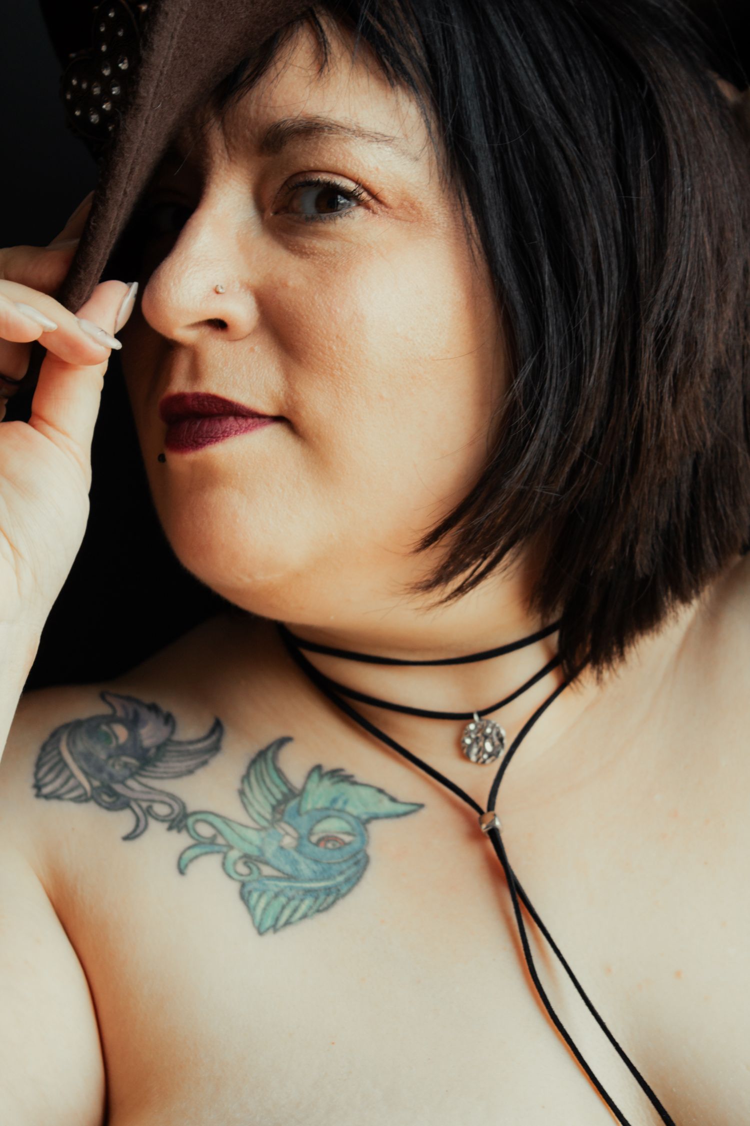 Close-up portrait showing a blue shoulder tattoo and black choker necklace.