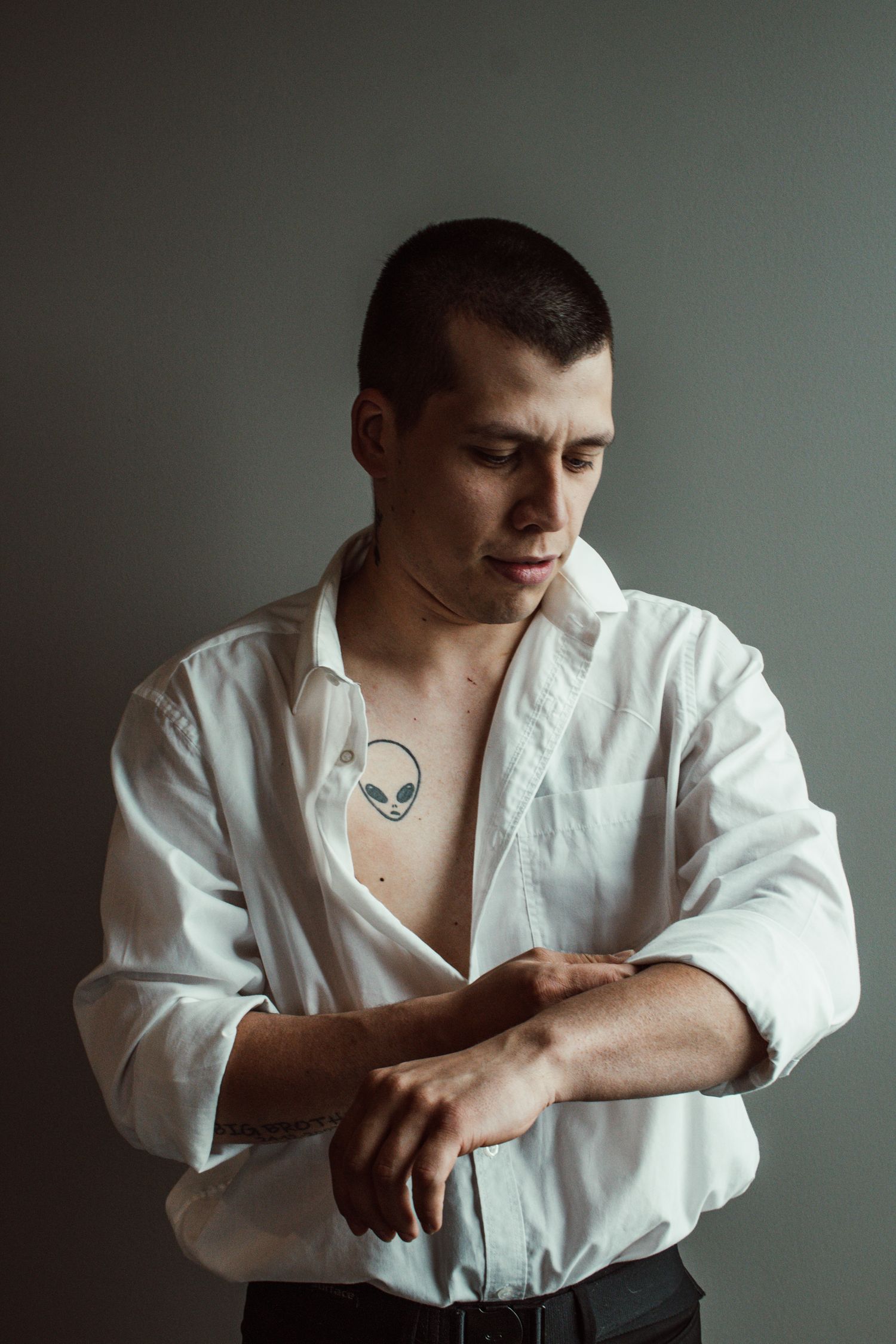 Person in white shirt with alien tattoo poses against grey background.