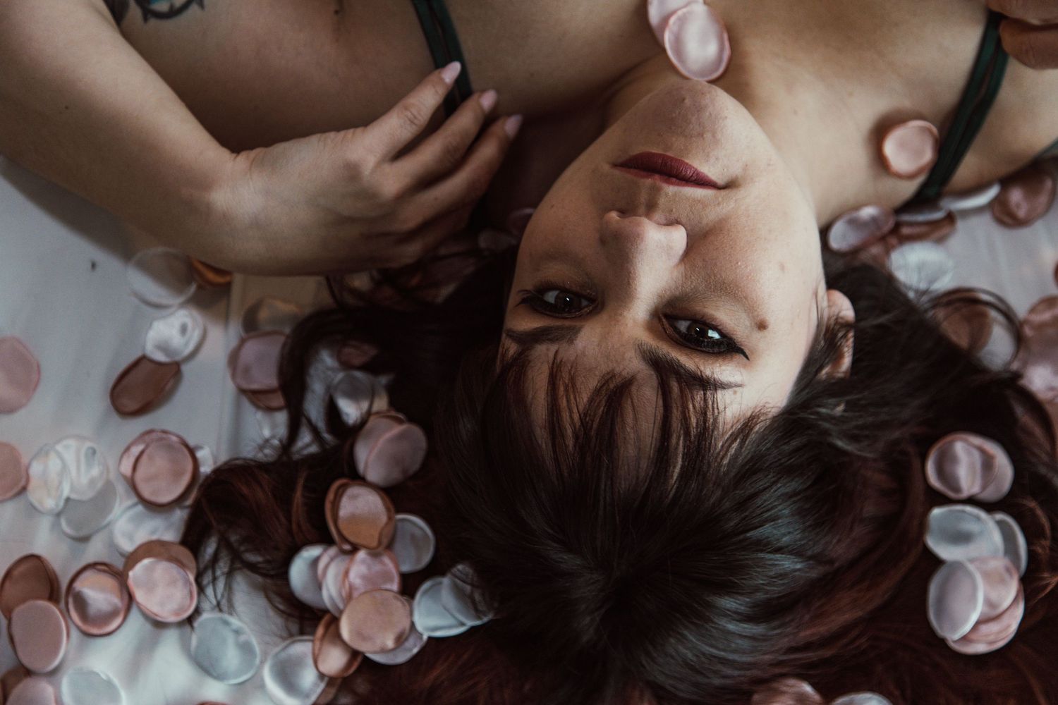 Artistic overhead boudoir photo with scattered pink rose petals and dark lingerie.