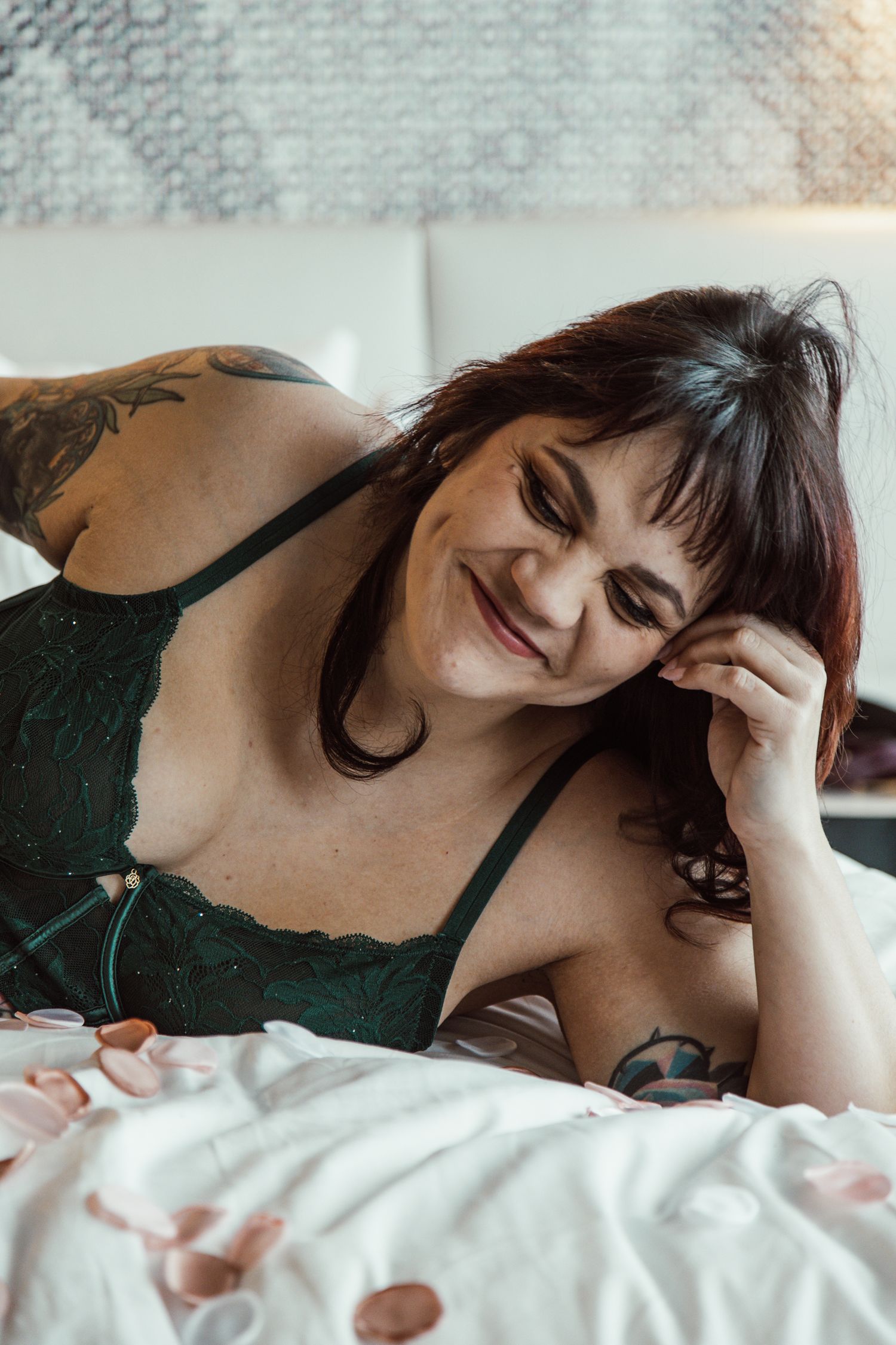 Intimate boudoir photography with figure in dark lace lingerie on white bedding.