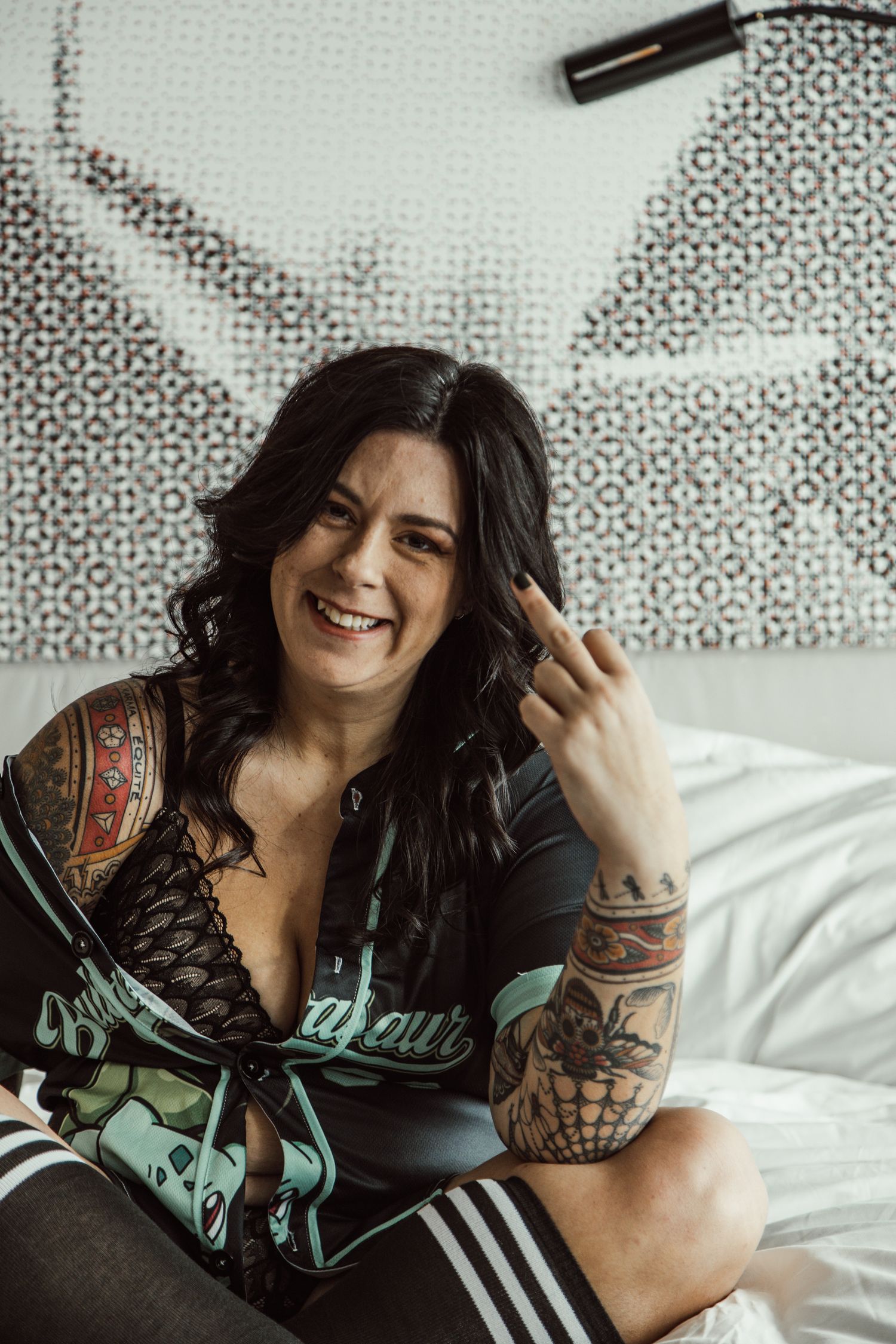Candid boudoir photo showing person with tattoos smiling on white bed.