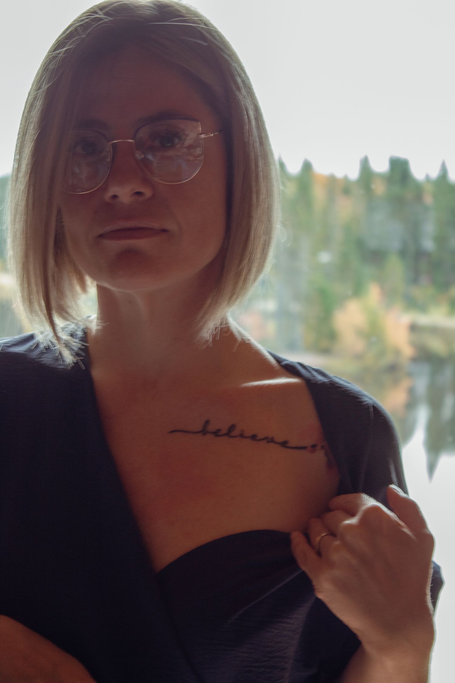 Portrait shot against window with lake and autumn trees visible outside.