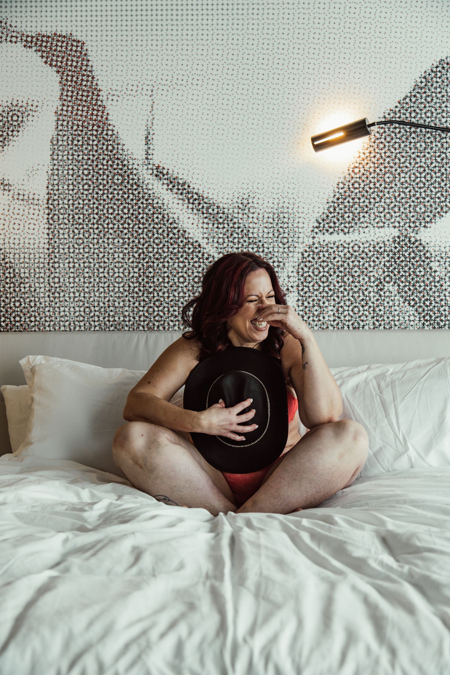 Candid lifestyle photo on white bedding with geometric wall art and modern lighting.