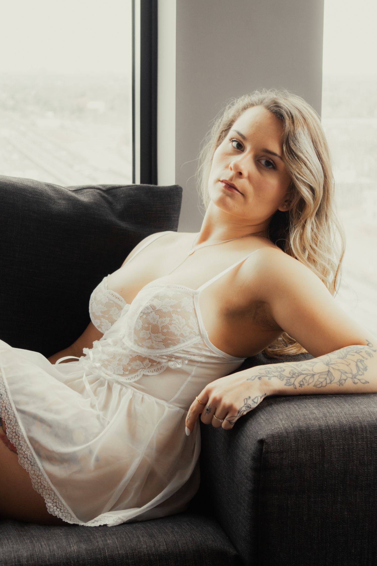 A series of boudoir photos showing someone in white lace lingerie reclining on a dark couch near a window.