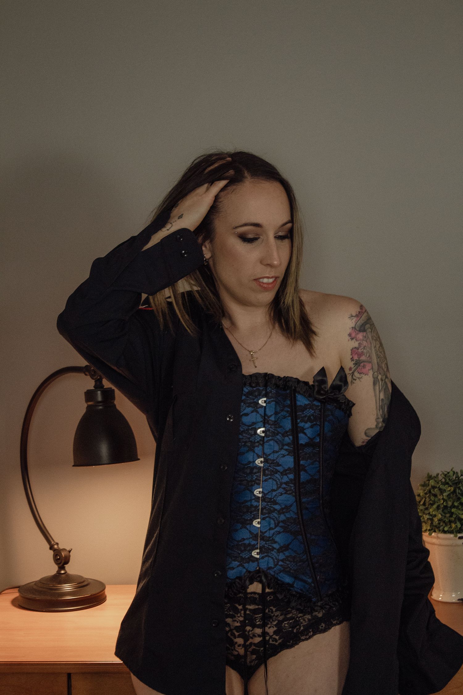 Figure in dark blue corset poses near a vintage lamp.