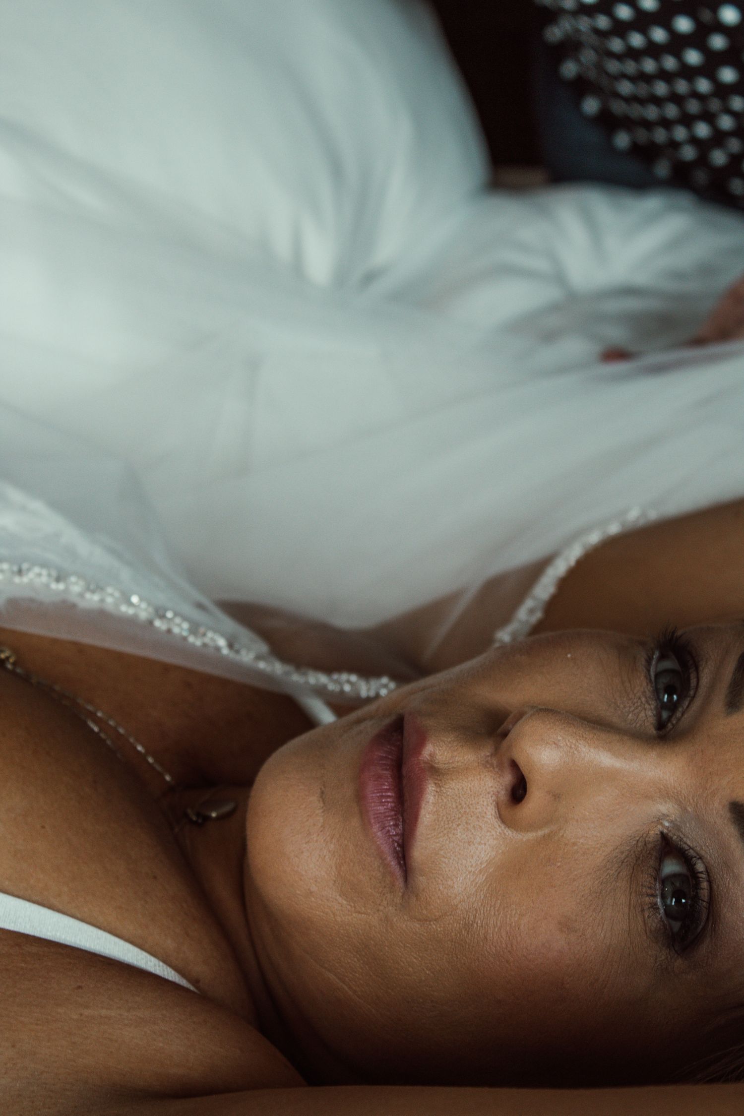 Close-up portrait on white bedding with soft lighting.