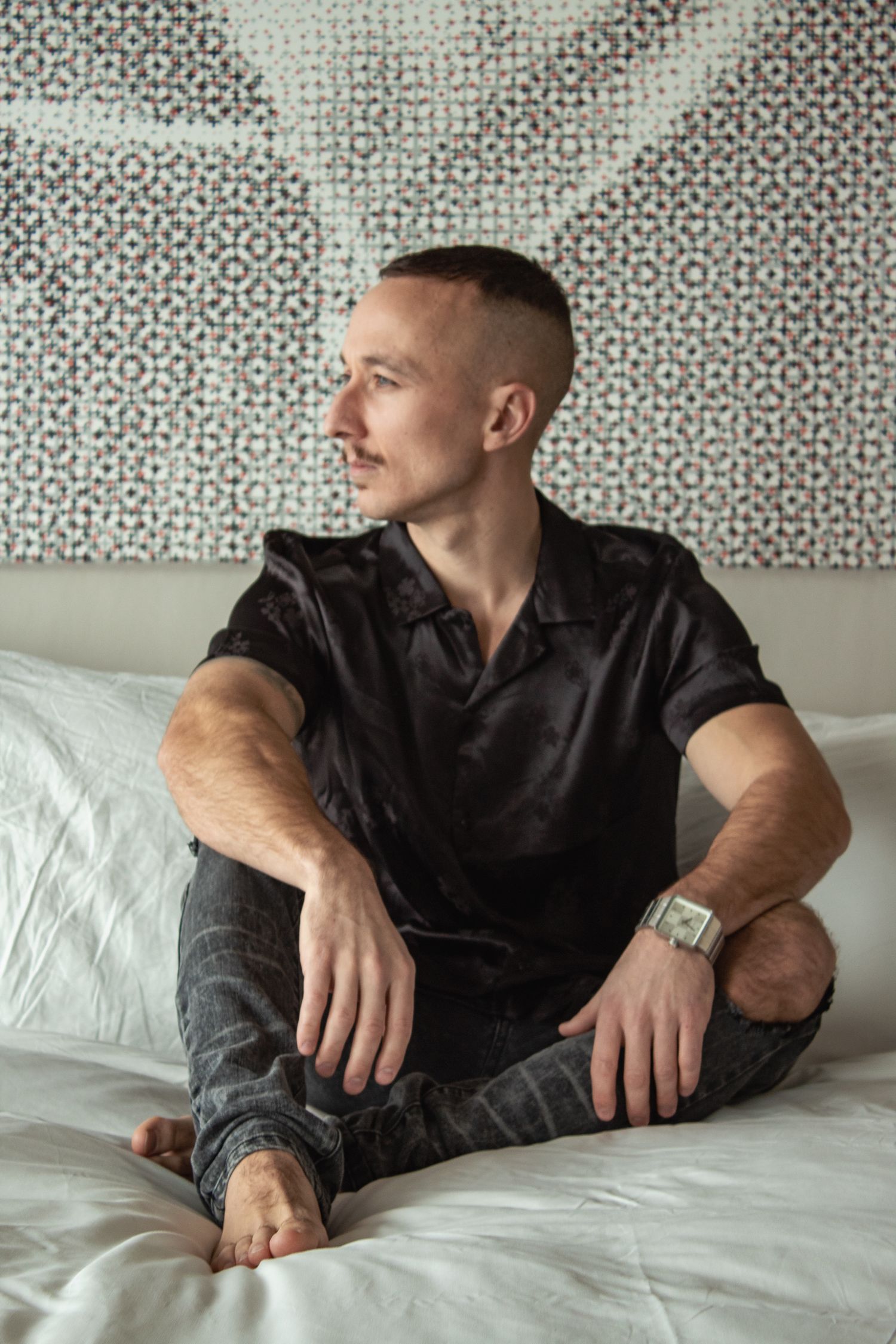 Person in black clothing lying on white bedding in a sequence of artistic poses.