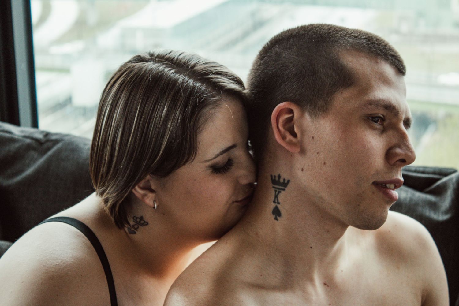 Intimate couple sharing tender moment by window with city view.