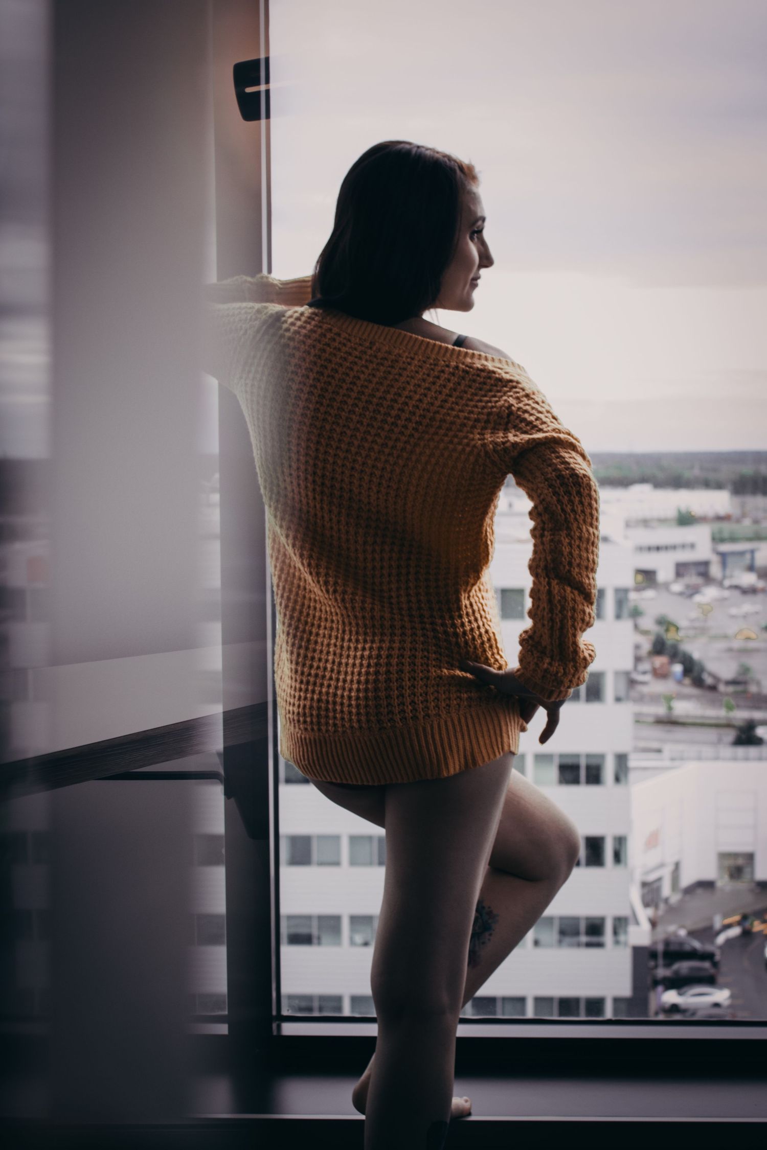 Silhouetted figure in brown sweater against window with cityscape view.
