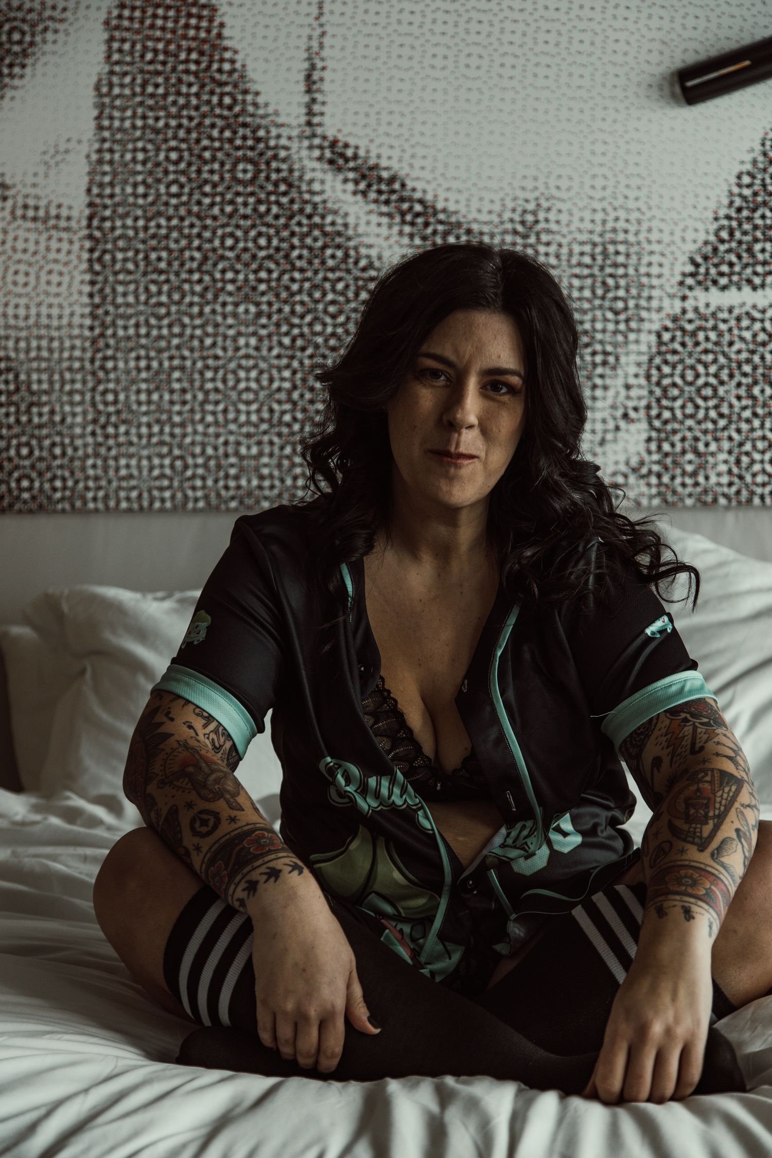 Artistic boudoir photo showing dark-haired figure in black and teal loungewear reclining on bed.