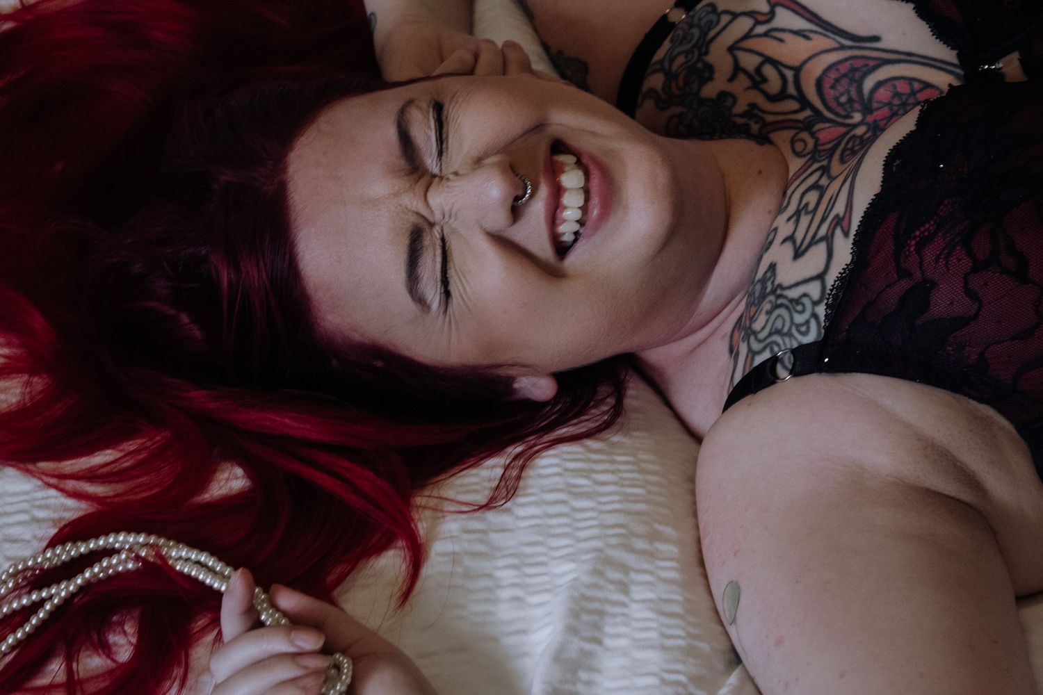 Artistic boudoir photos with red tones showing intimate poses on white bedding.