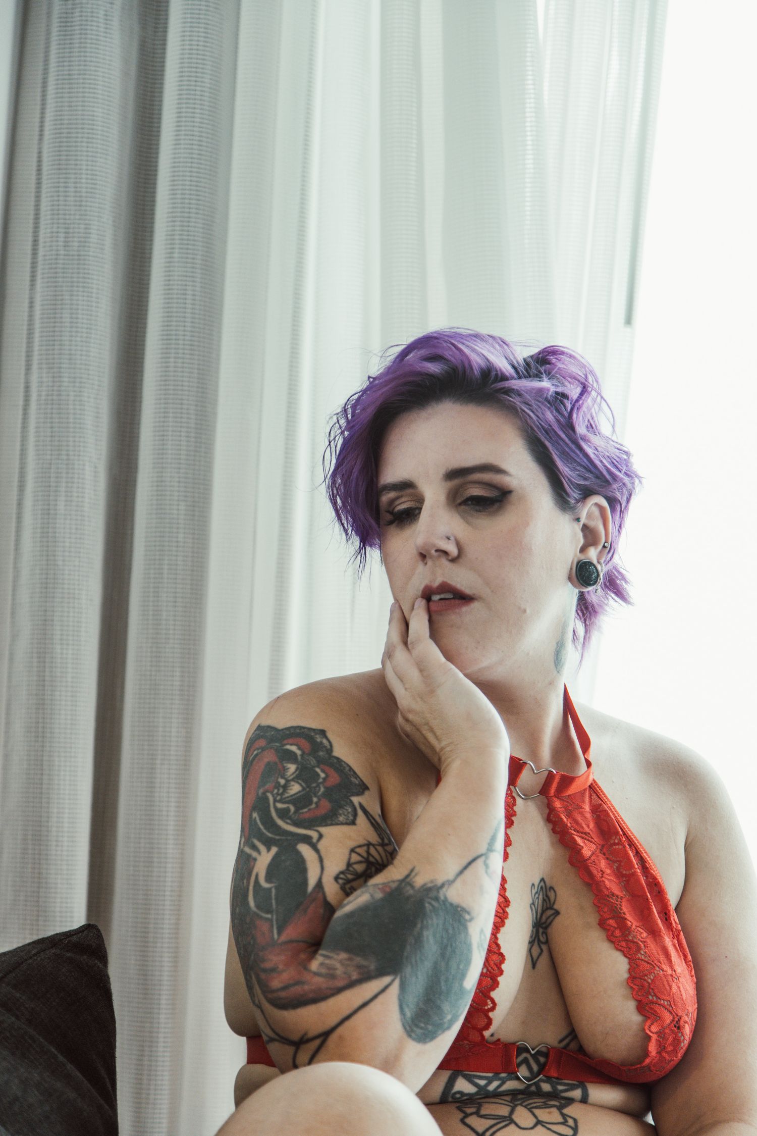 Moody boudoir portrait with red lingerie and visible tattoo art.