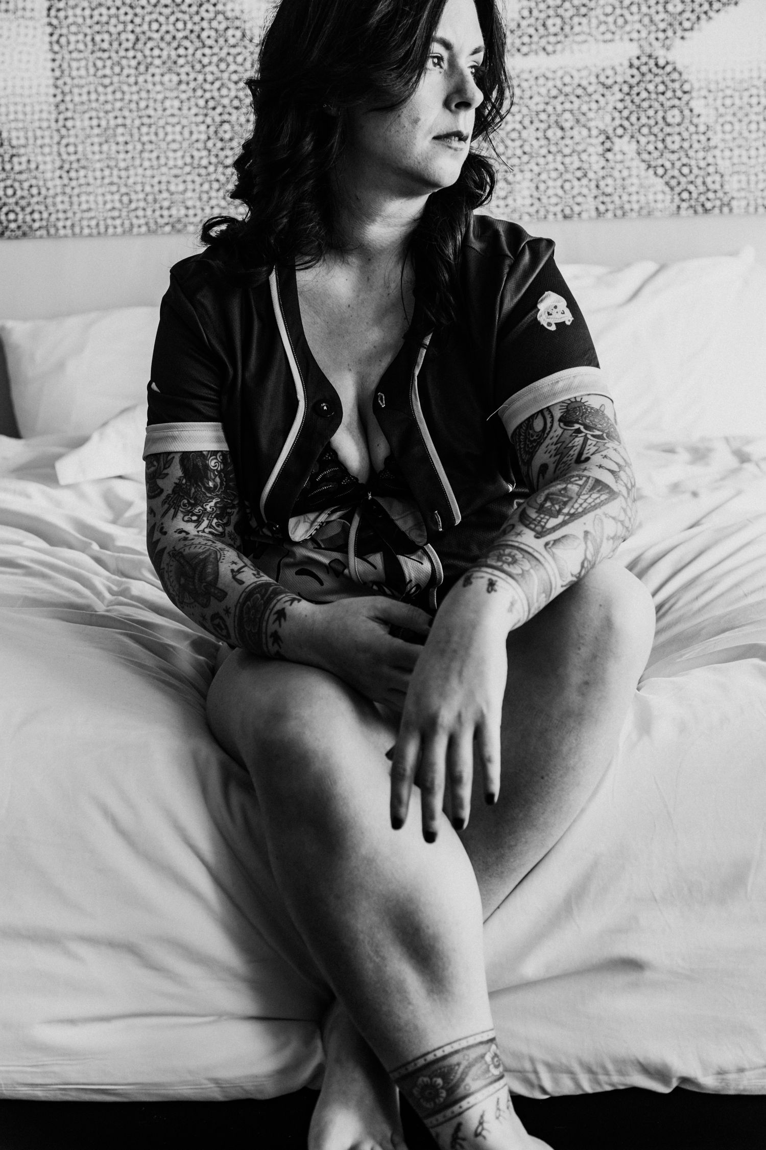 Black and white boudoir photo showing person reclining on white bedding.