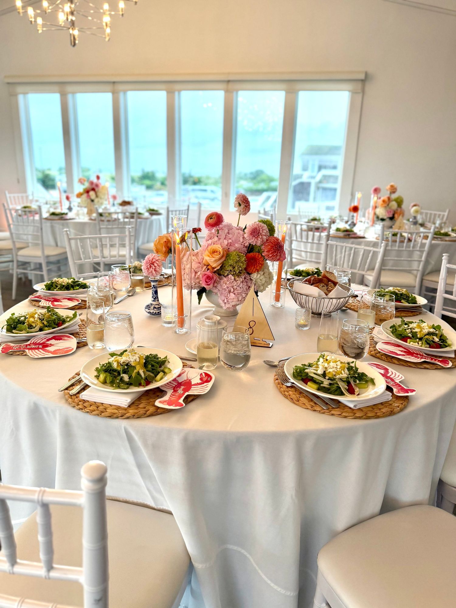 Elegant wedding reception table with white linen, wicker chargers, salad plates, and pink floral centerpiece in bright coastal venue.