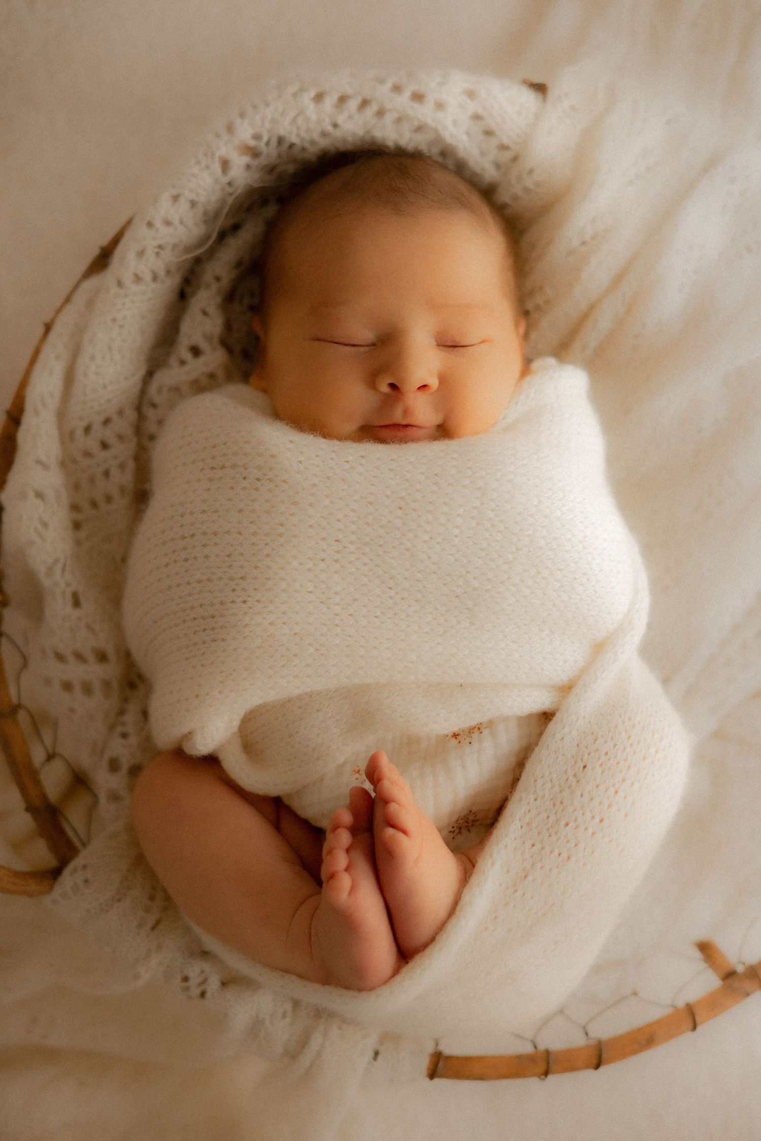 Séance photo nouveau-né lifestyle à Montréal, bébé paisiblement endormi emmailloté dans une couverture blanche sur un fond en dentelle délic