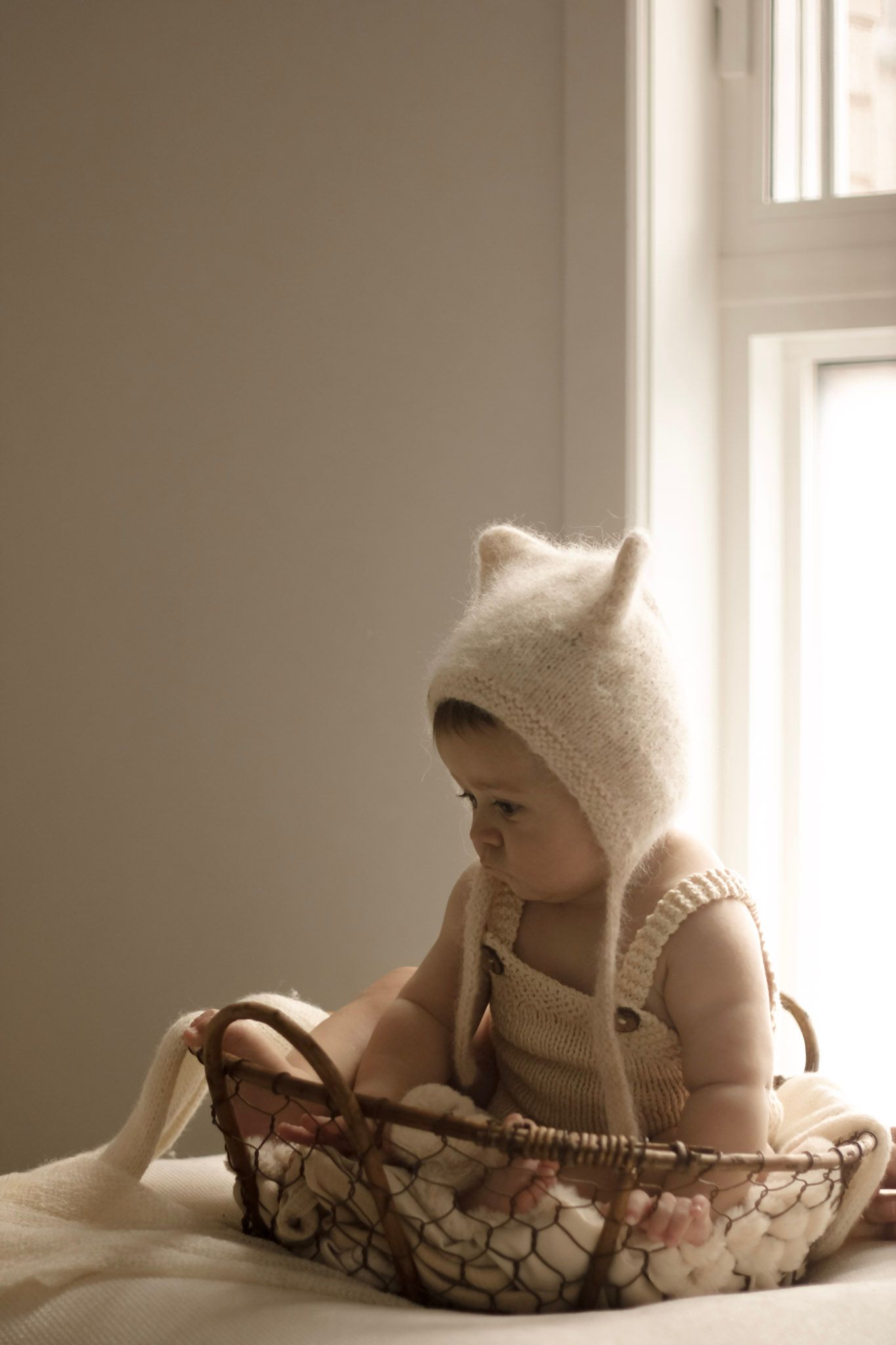 Bébé en vêtements blancs en tricot assis dans un panier tissé, photo en léger flou