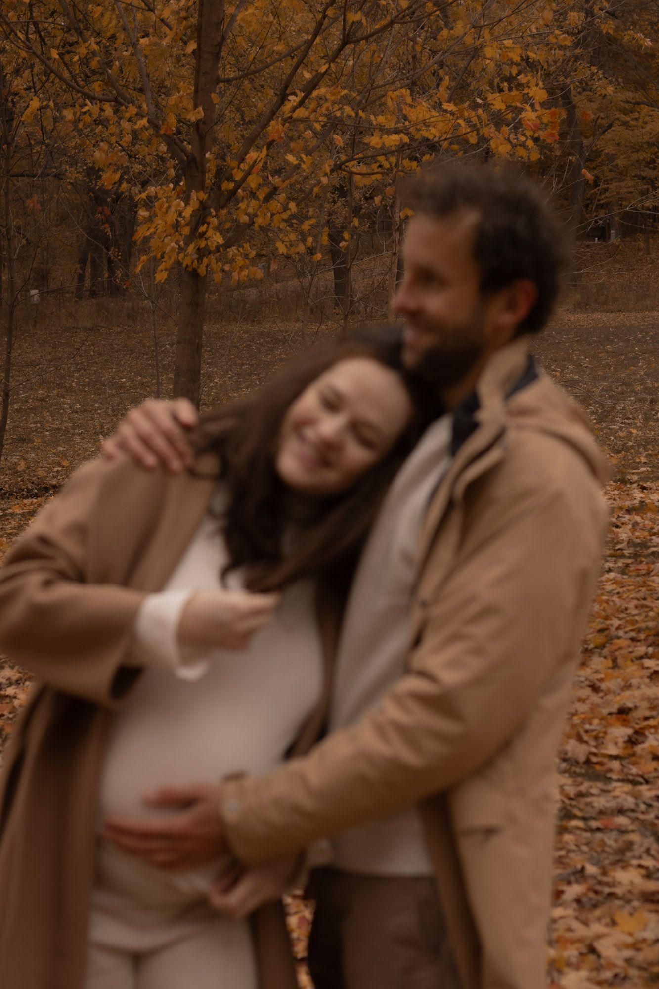 Couple en séance photo à Montréal, partageant un instant joyeux sur les feuilles tombées dans la forêt.
