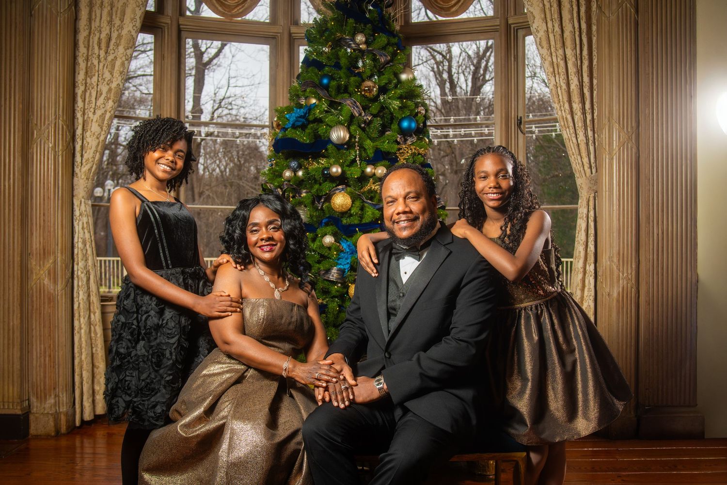 Elegant family of four posing in formal attire beside a decorated Christmas tree.