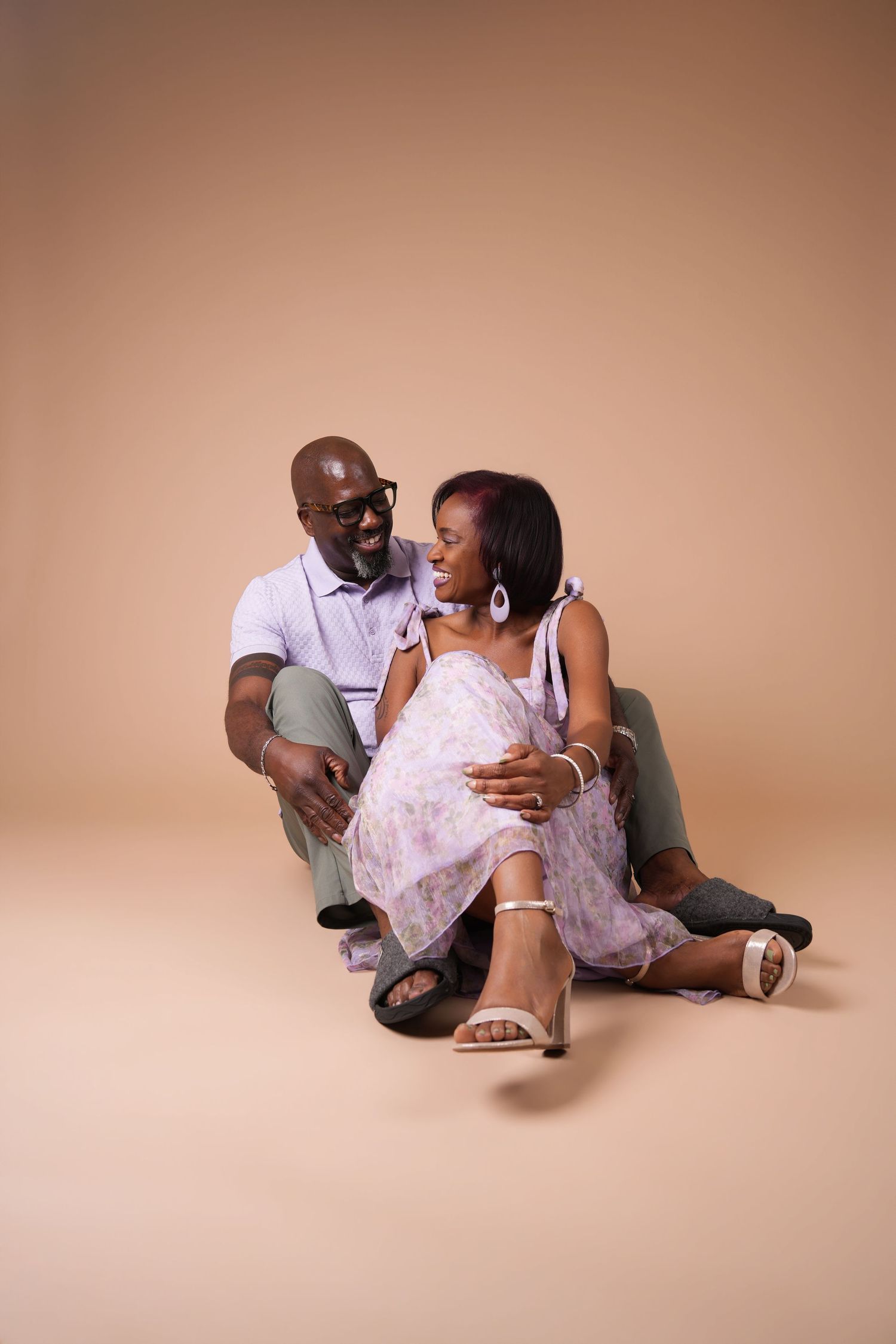 Happy couple sharing a laugh during a studio couples photoshoot in Charlotte, NC, seated together on the floor against a warm beige backdrop