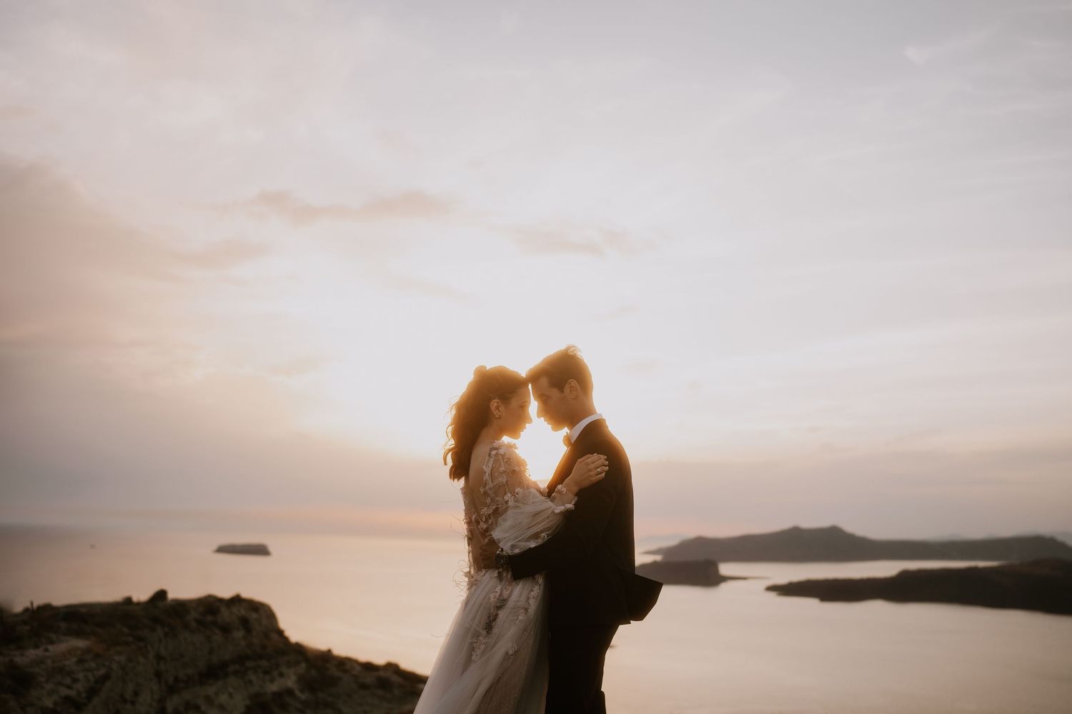 A romantic silhouette of a couple embracing at sunset on a beach with mountains and ocean in the background.