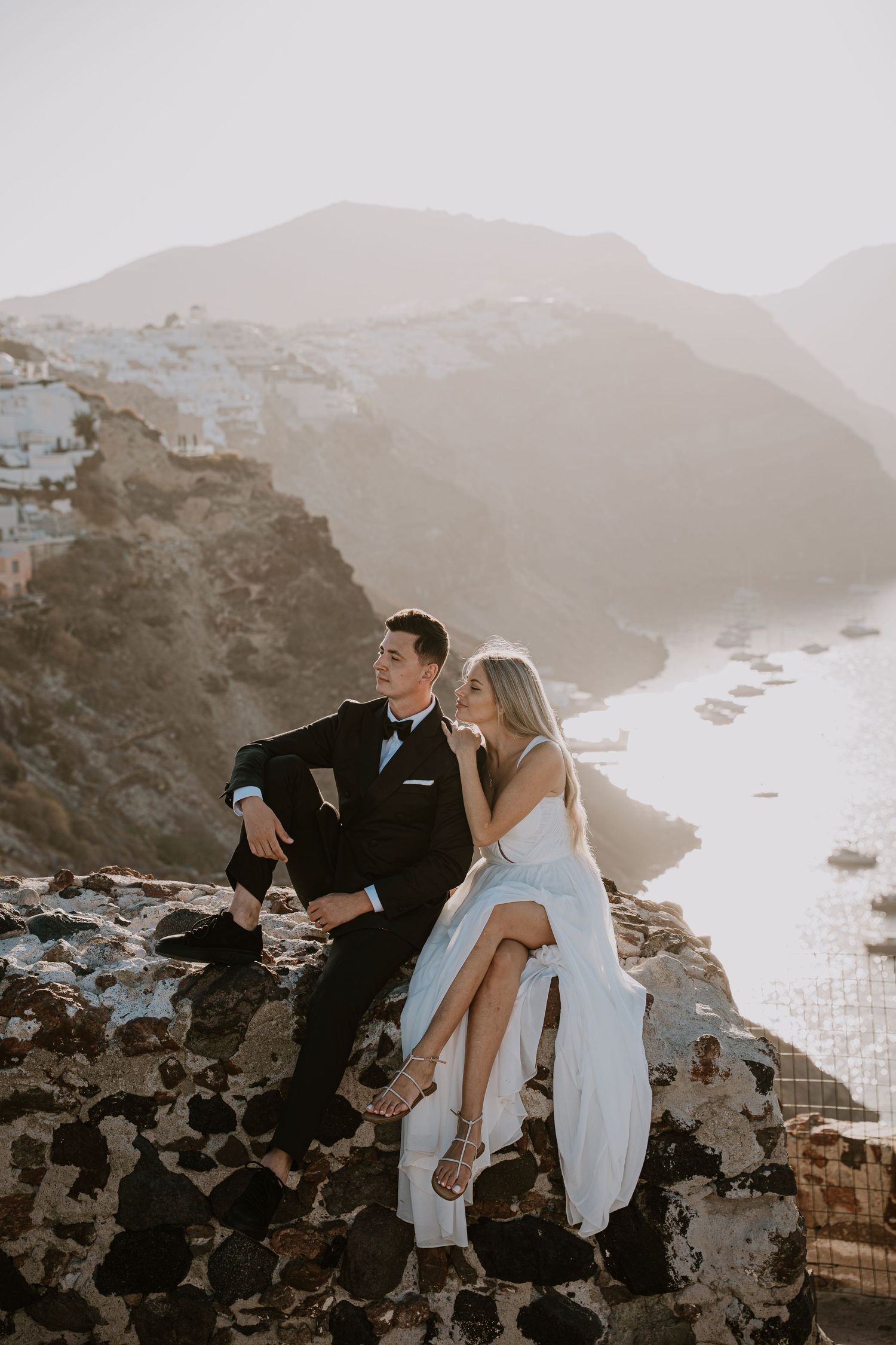 A dreamy wedding photoshoot on rocky cliffs overlooking a Mediterranean coastal town at sunset.