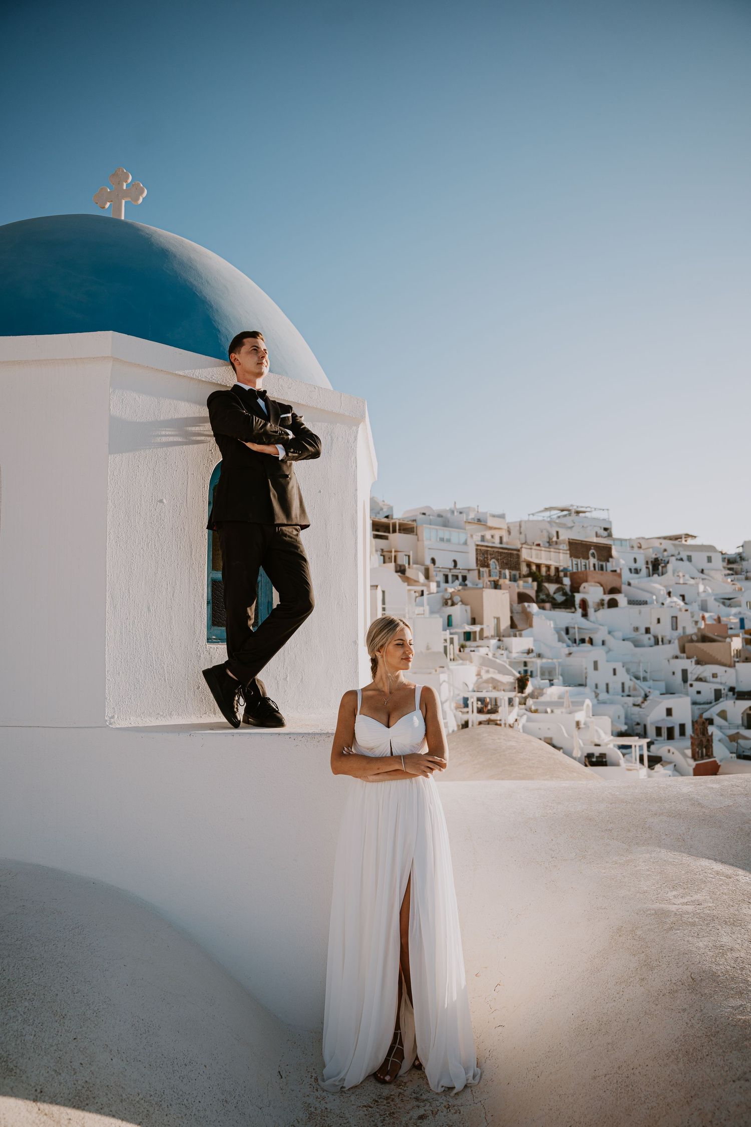 Creative wedding portrait with couple posed at different levels by Santorini church dome.