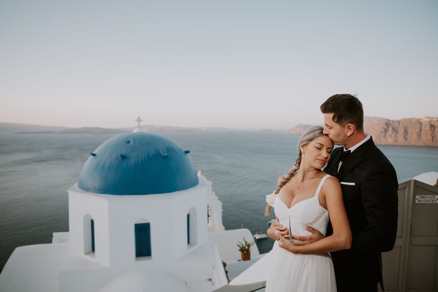 Wedding couple poses by iconic blue-domed church in Santorini with ocean views.
