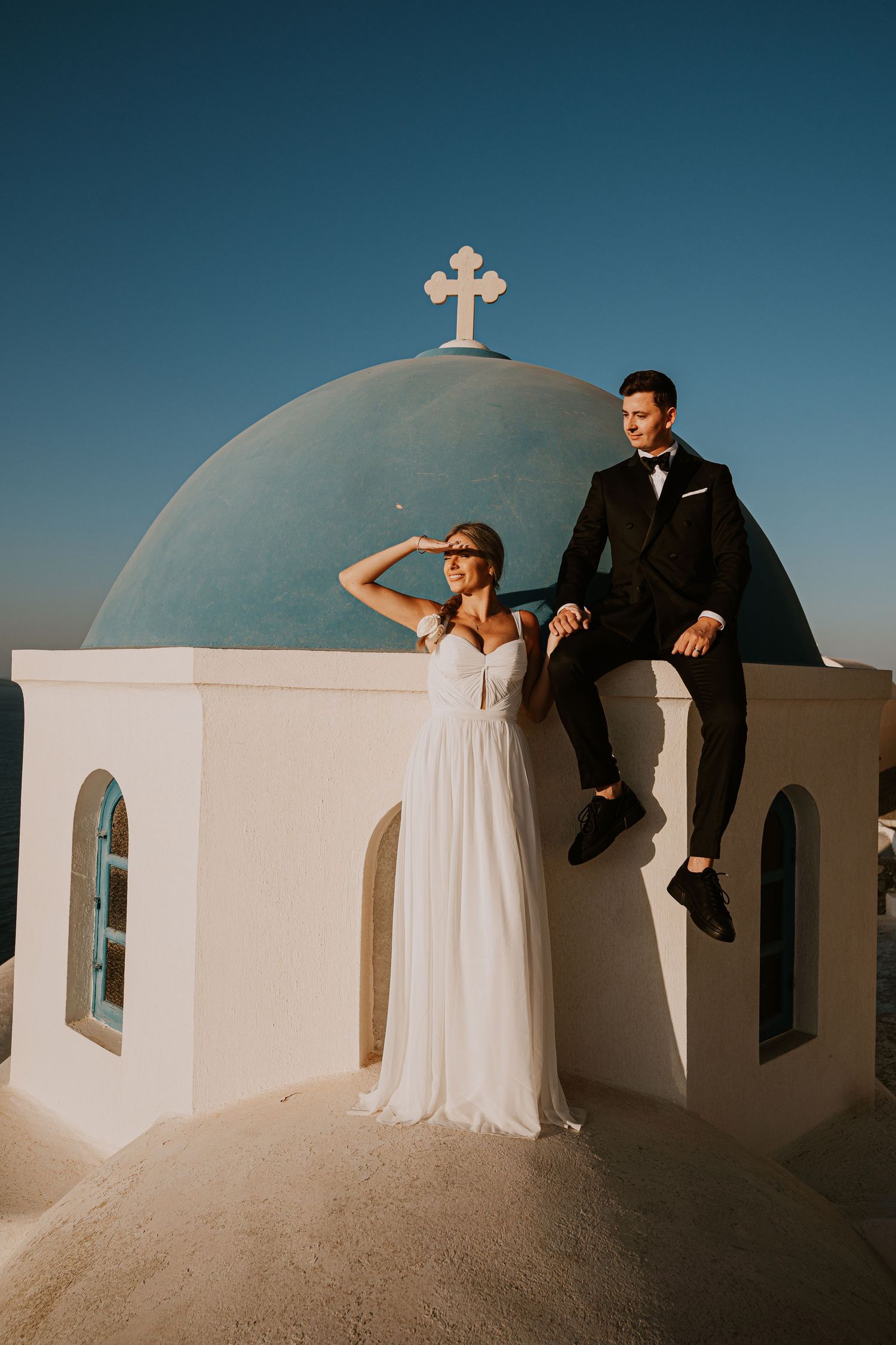 A romantic photoshoot at a white Mediterranean church with blue domes and a cross.