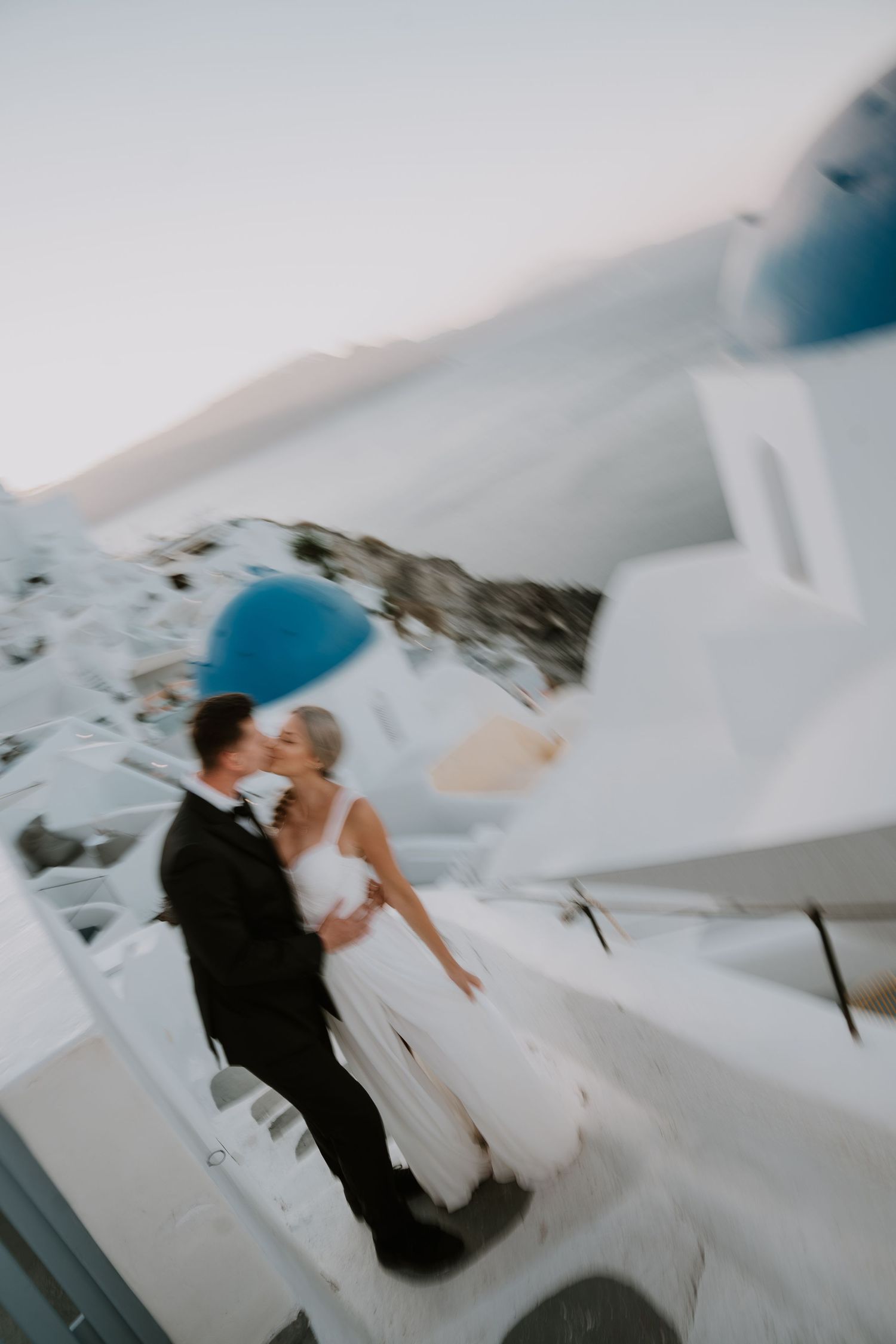 Artistic tilted shot of newlyweds among Santorini's white architecture and blue domes.