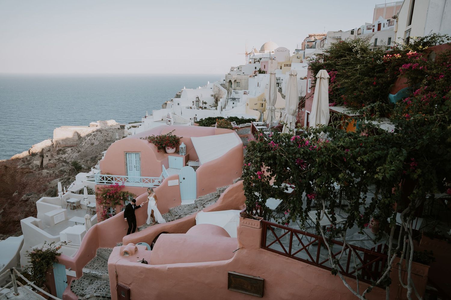 A scenic view of Santorini's white and pink buildings cascading down the hillside towards the blue Aegean Sea.
