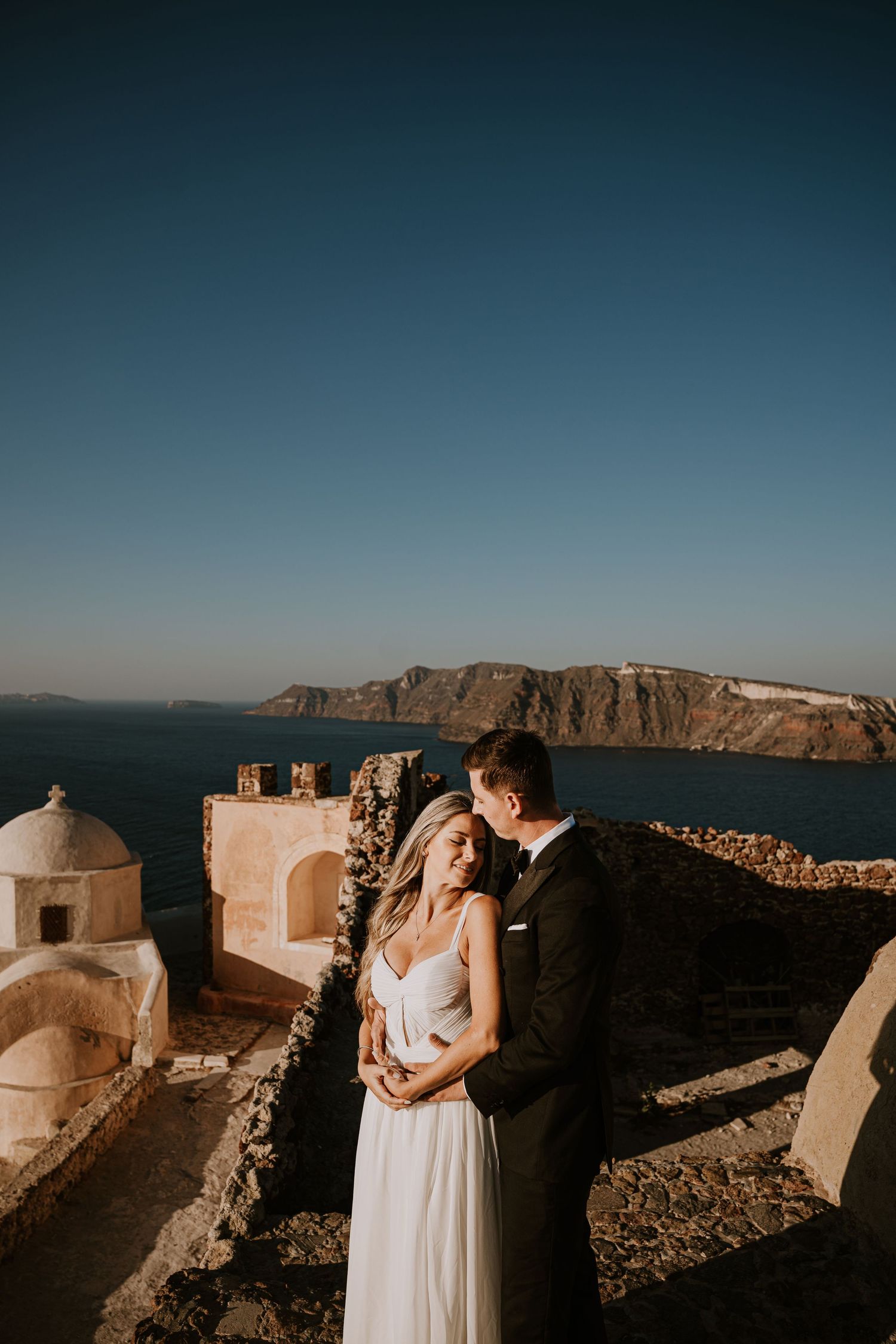 A seaside wedding photoshoot with dramatic coastal cliffs and white architecture in the background.