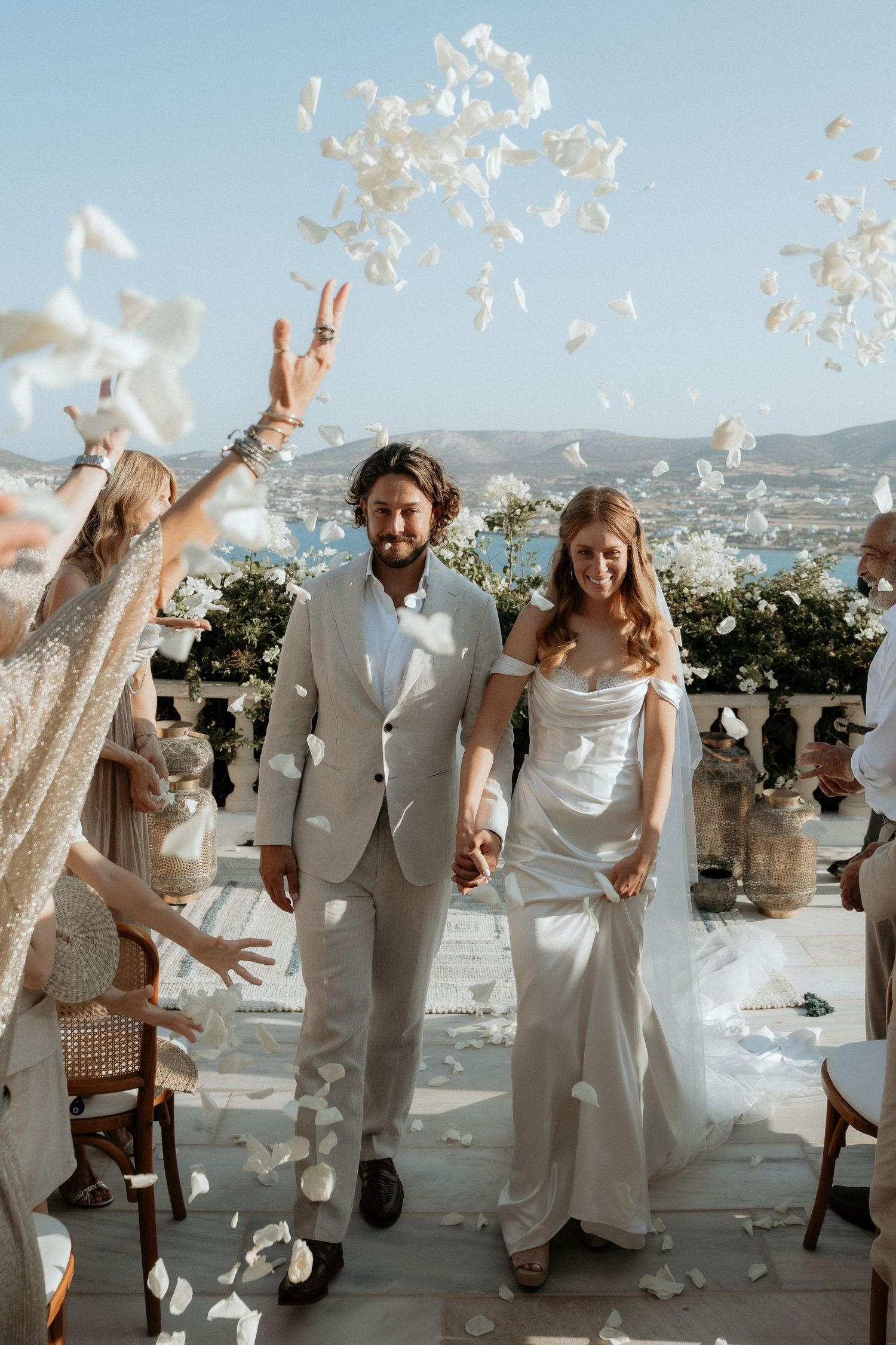 Wedding party throws white feathers in celebration during outdoor reception with mountain backdrop.