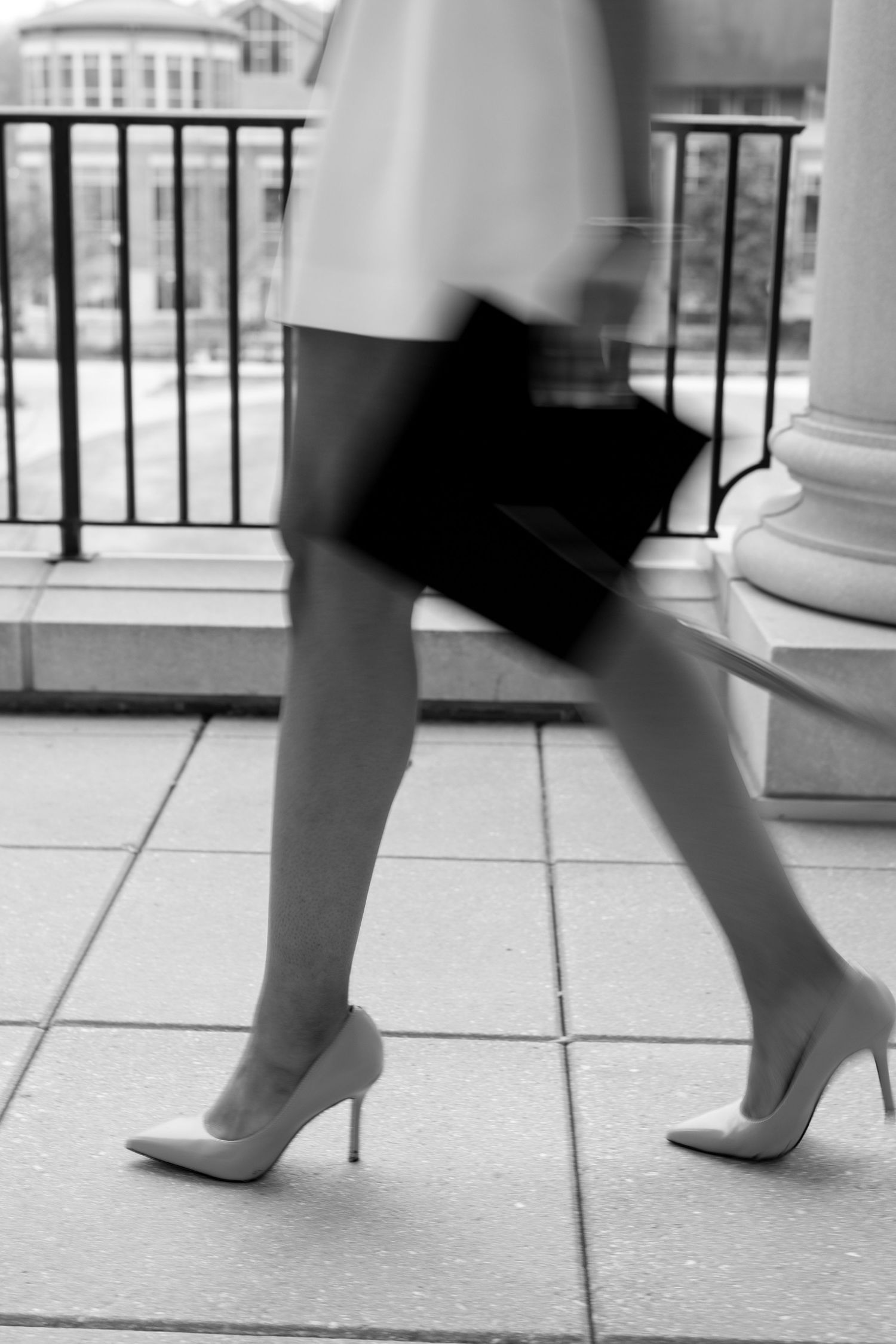 Black and white sequence of feet in heels walking across a tiled surface.