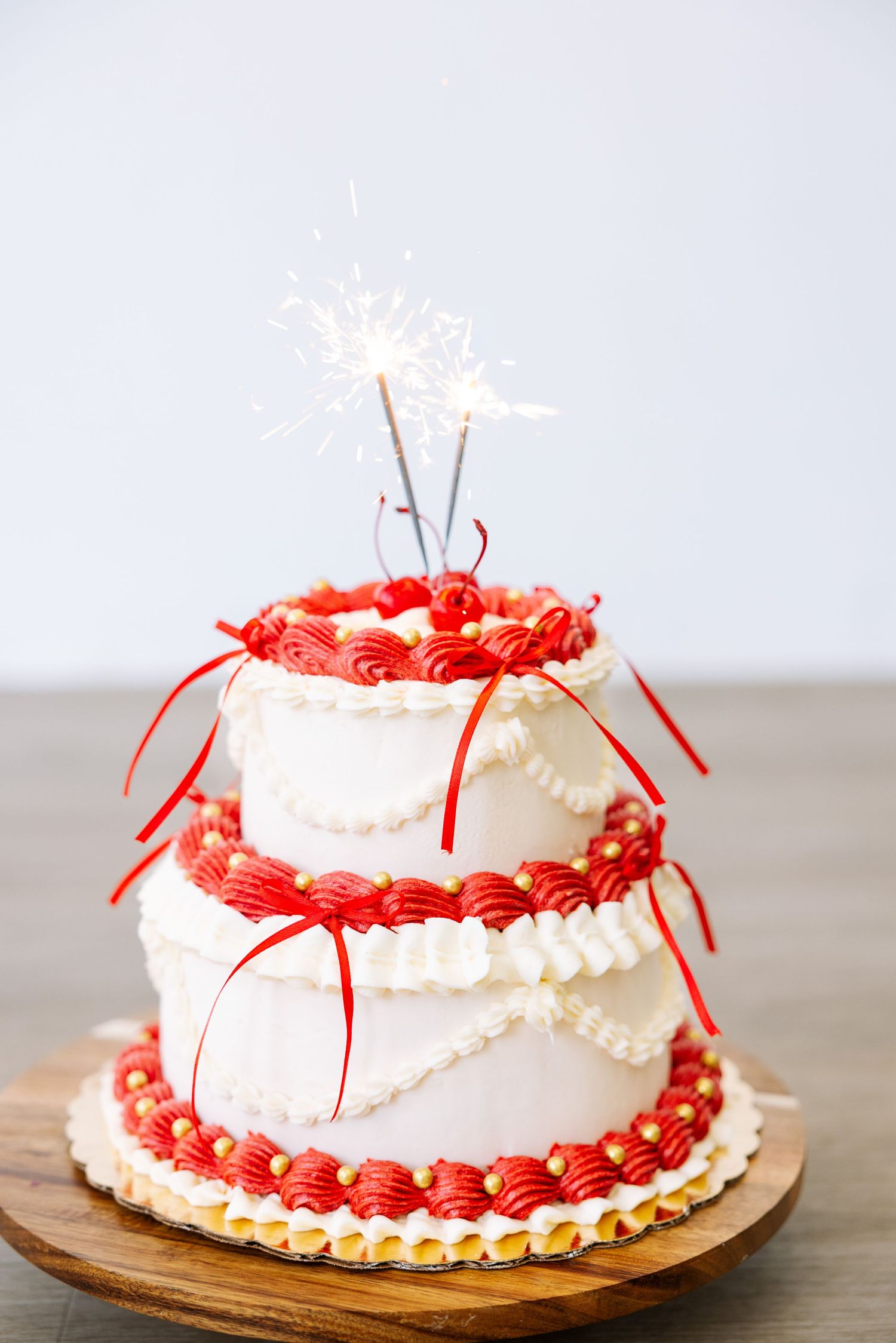 White and red tiered cake with sparklers on wooden board against white background.