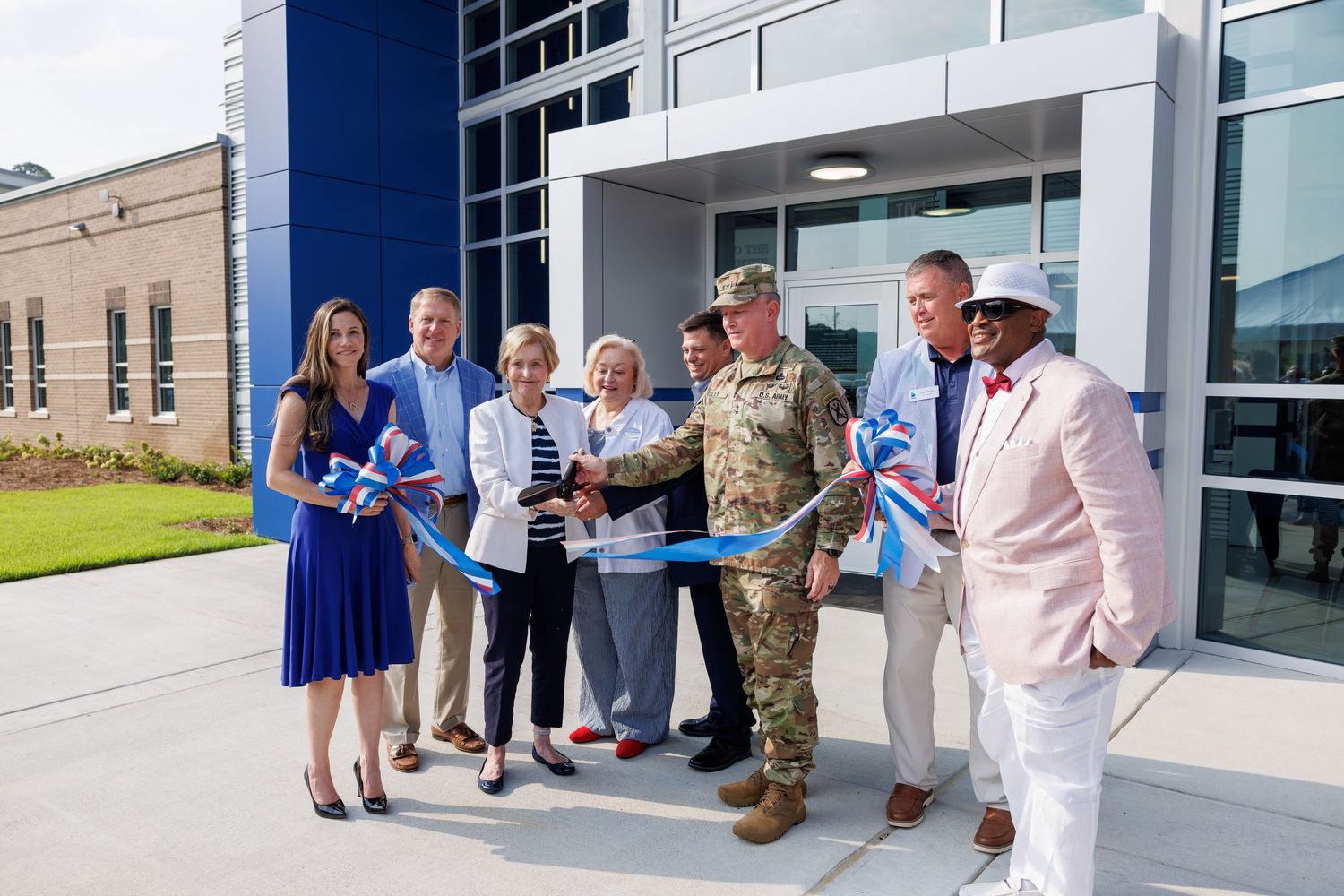 Military officer and officials cut ribbon at modern building grand opening ceremony outdoors.