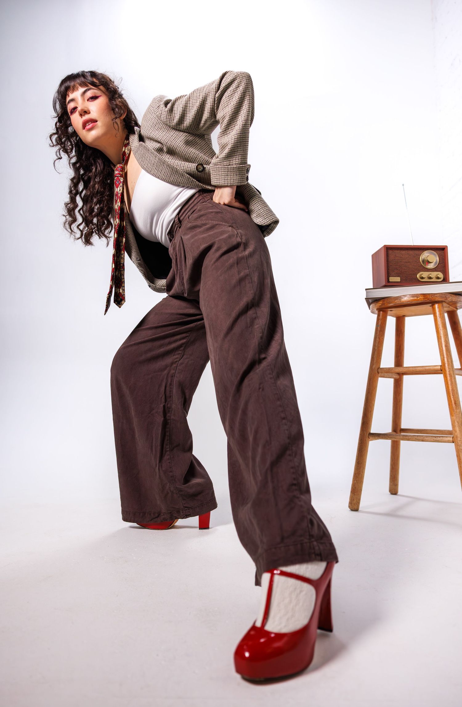 Studio fashion photos featuring brown wide-leg pants and red shoes with a wooden stool prop.