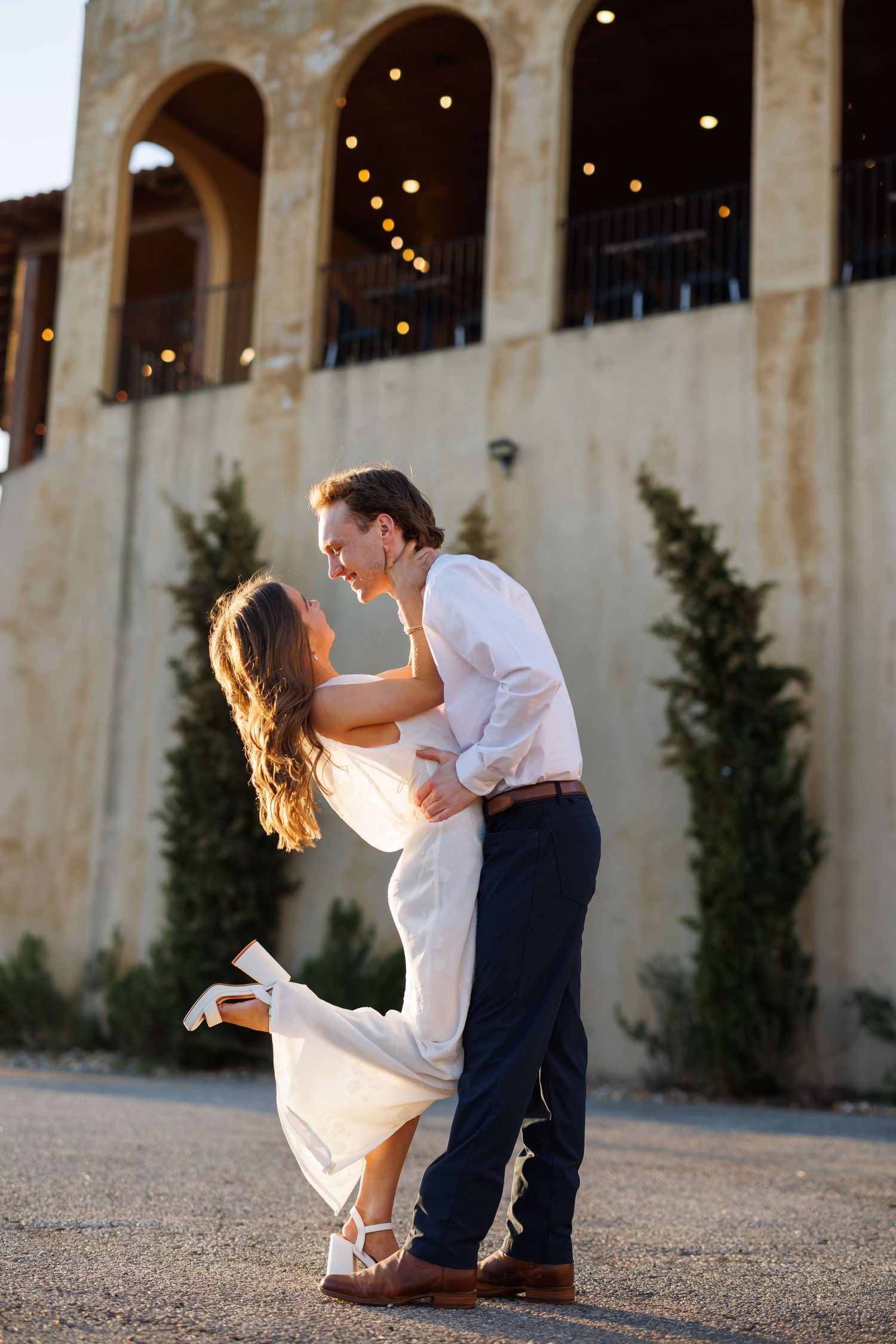 Dancing couple in formal wear spinning on gravel courtyard with Mediterranean architecture.