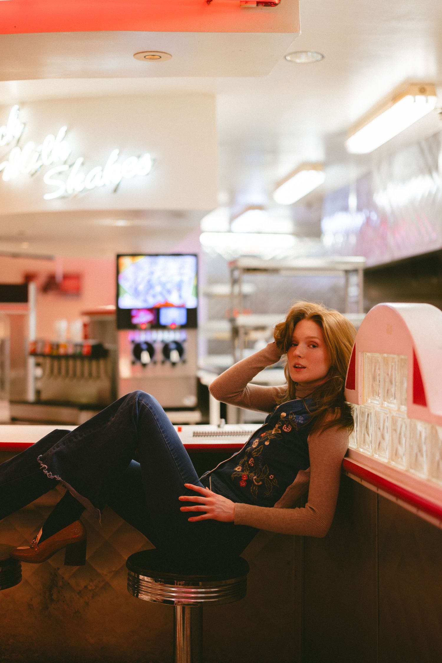 Woman relaxes on vintage diner counter seating in casual attire.