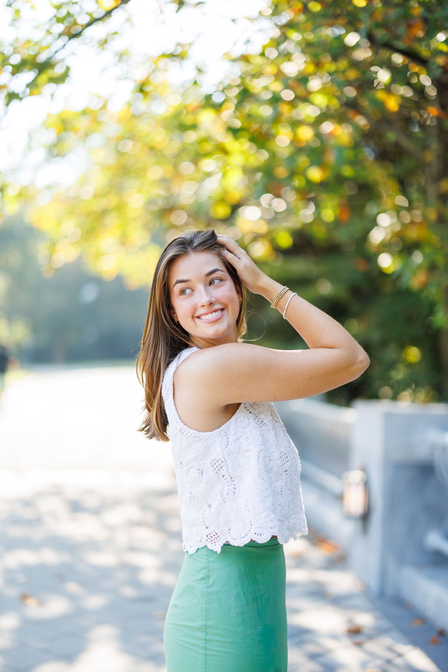 Woman in white lace top and mint green skirt poses outdoors with natural bokeh background.