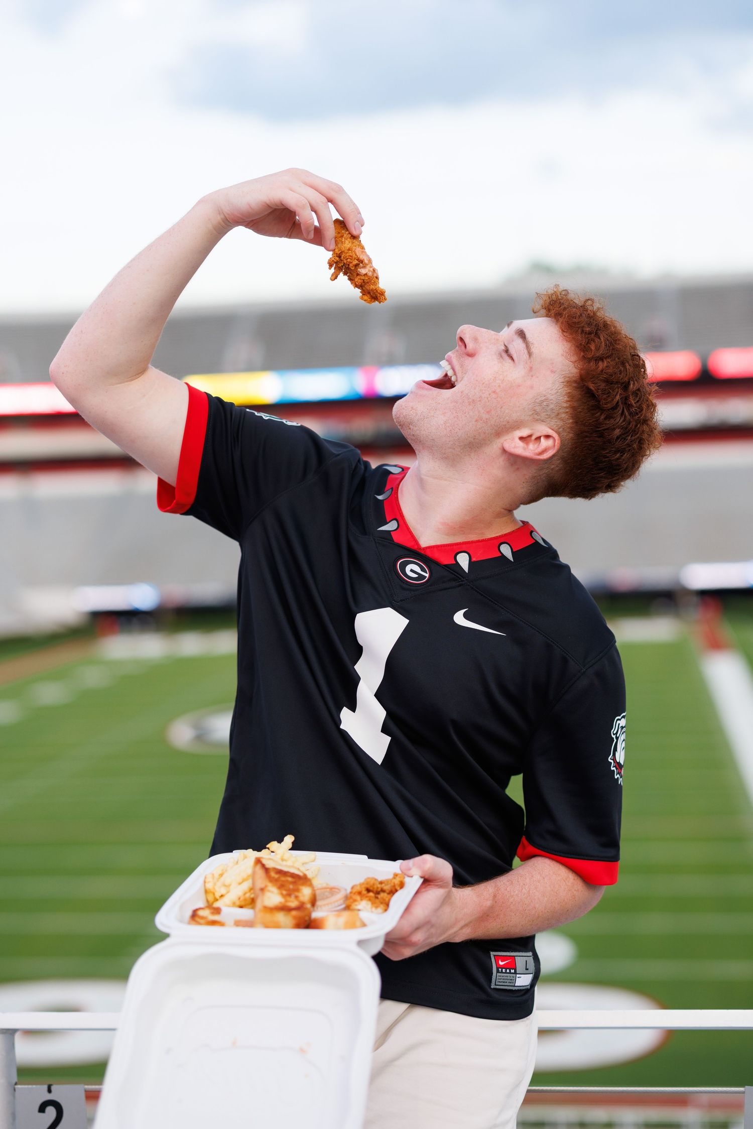 Person in black shirt dramatically eating Cane's chicken tenders at a football stadium.