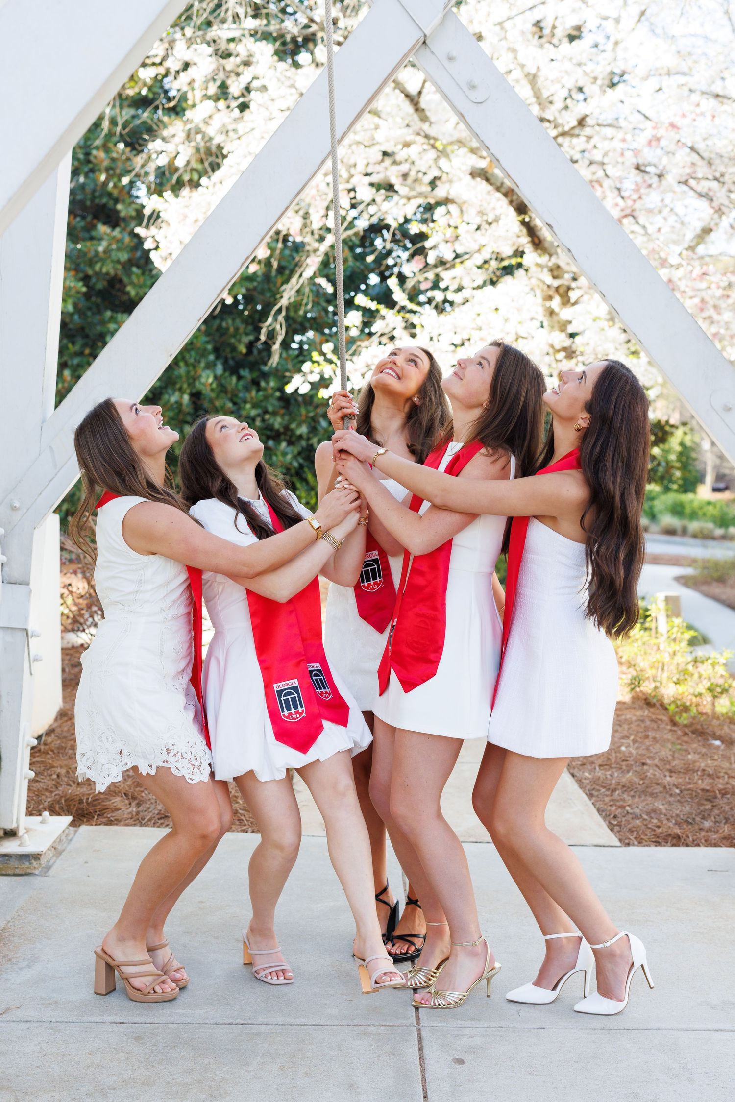 A group of women in red and white outfits lean back together in a playful pose under a white gazebo.