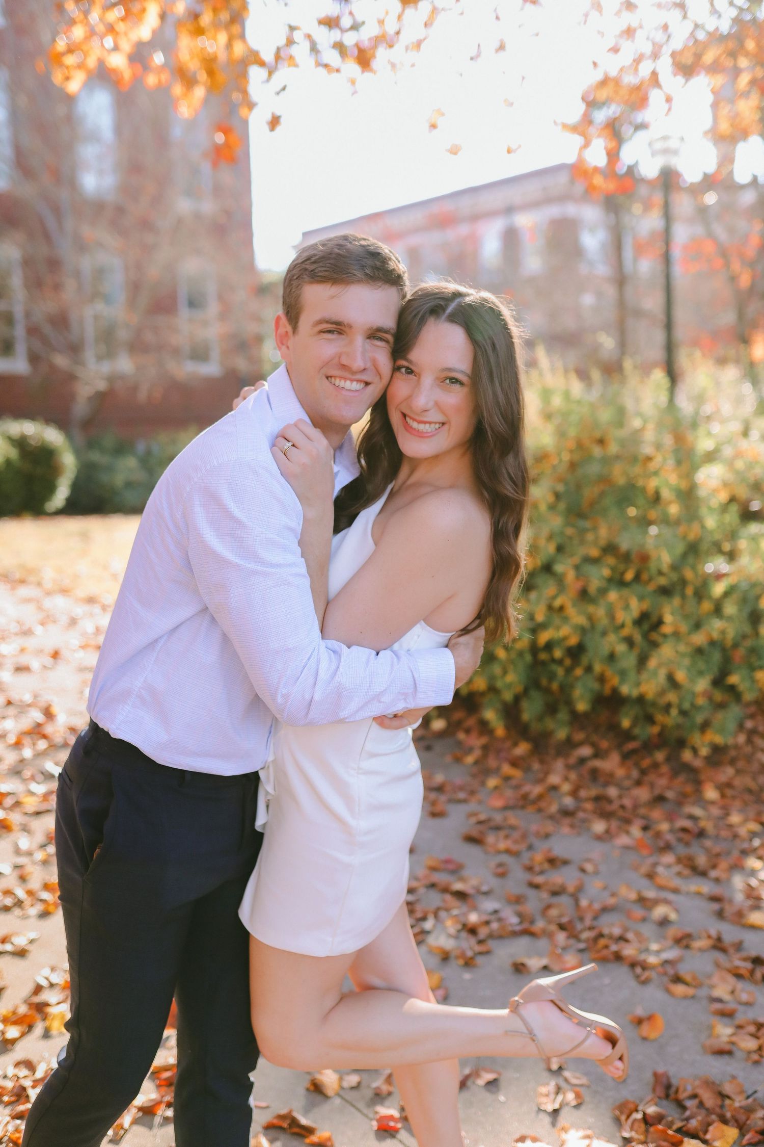 A couple shares a playful moment together on a fall day with orange leaves in the background.